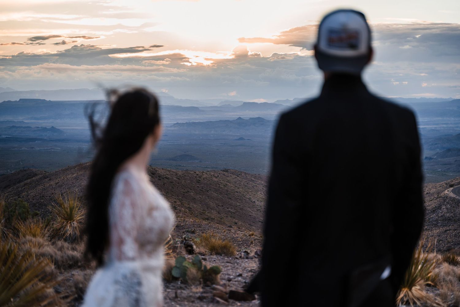 A couple in wedding attire silhouetted against a mountainous sunset landscape.