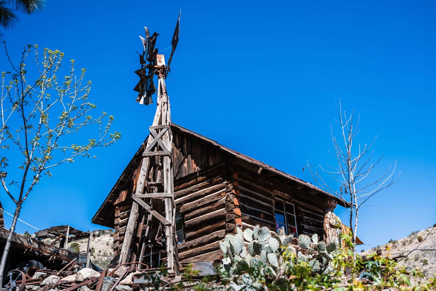 Rustic log cabin with angel statue perched on top against bright blue sky at Jack Kerouac's Shrine in Rocky Mountains.