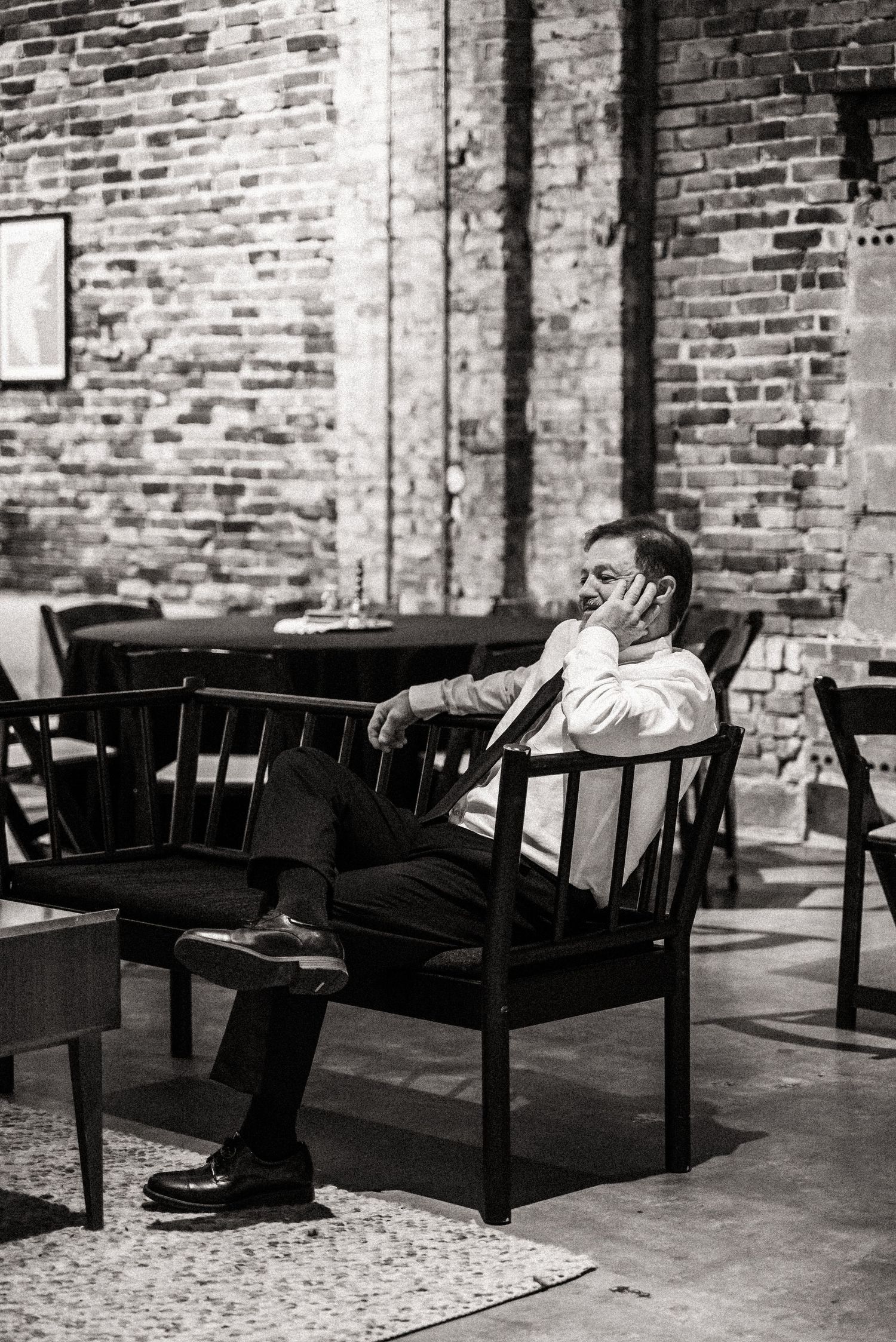 A black and white photo shows someone sitting alone in a chair against an exposed brick wall.