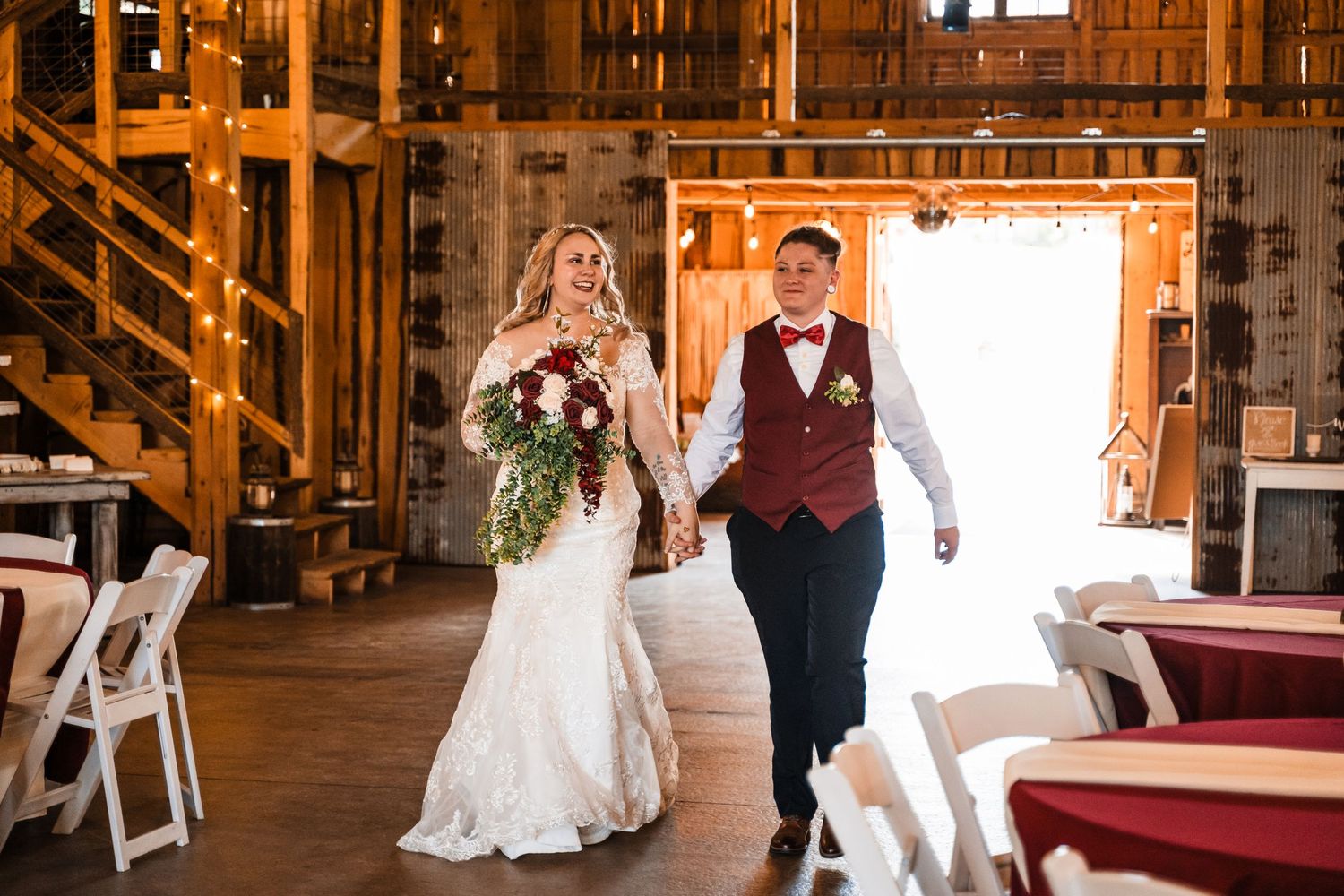 Couple walks hand in hand inside rustic wooden barn venue after their wedding ceremony.