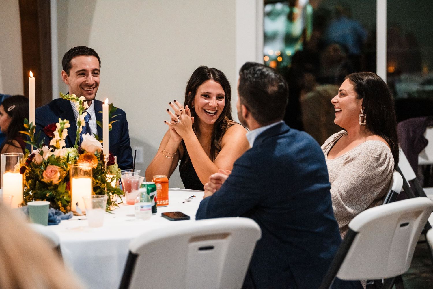 Wedding guests engage in lively conversation at a candlelit reception table.