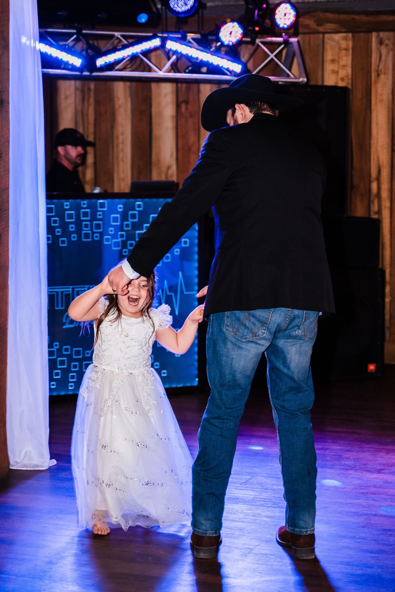 A touching father-daughter dance moment at a wedding reception with blue lighting and wooden walls.