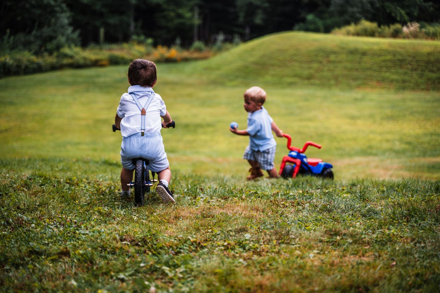 Two children playing with ride-on toys in a grassy field.