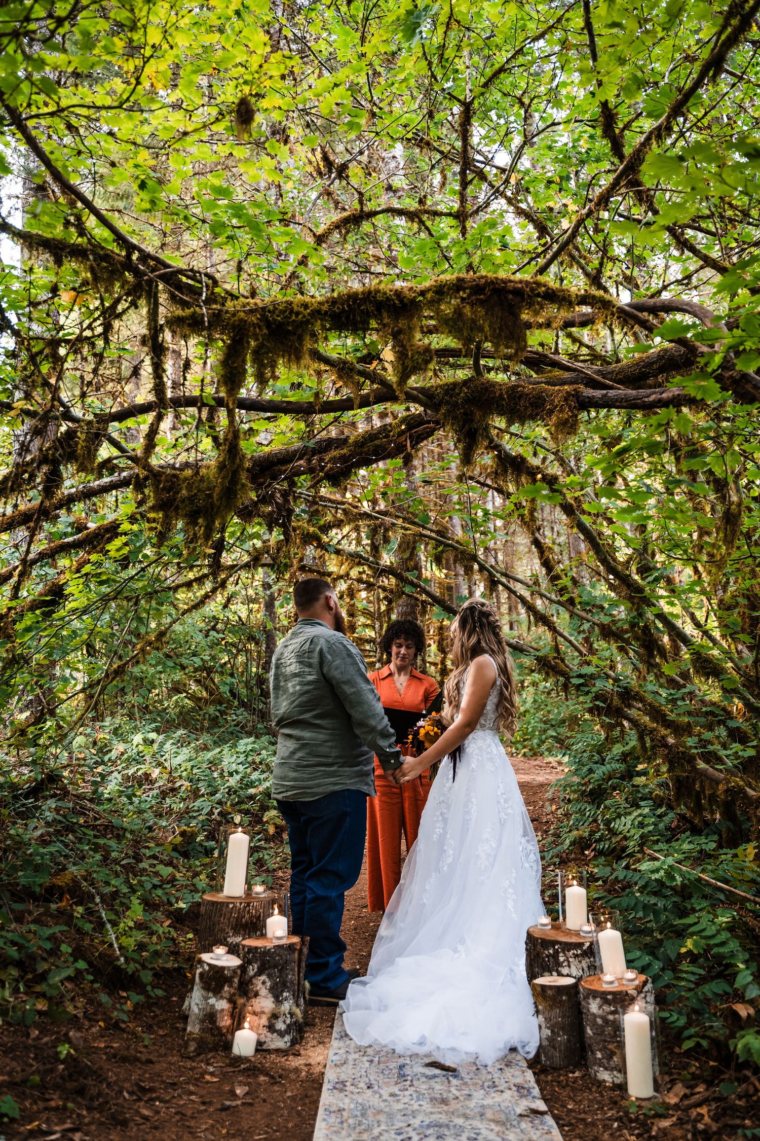 Forest wedding ceremony setup with candles on wood stumps under moss-covered branches.