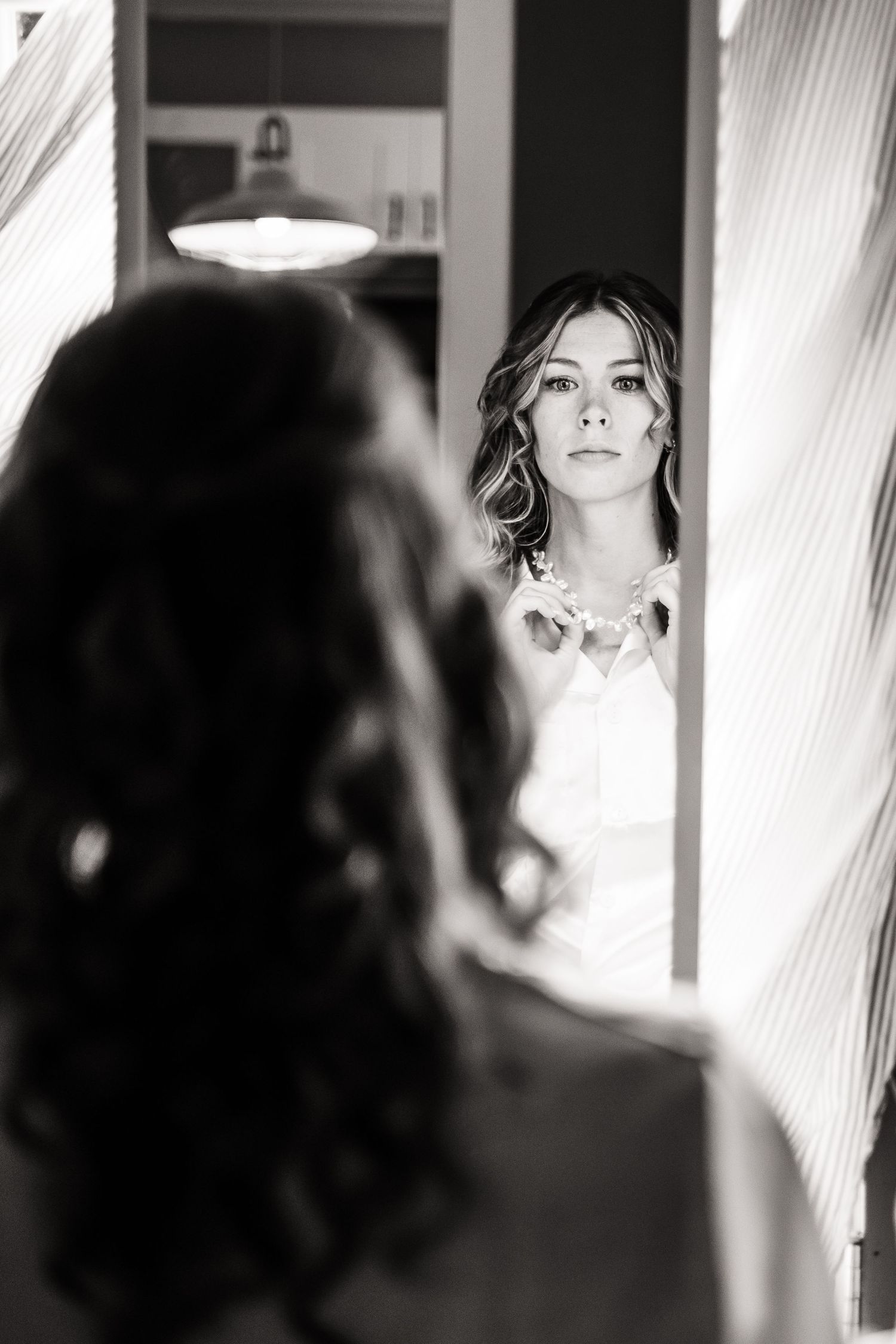 Artistic black and white reflection of bride looking in mirror while getting ready.