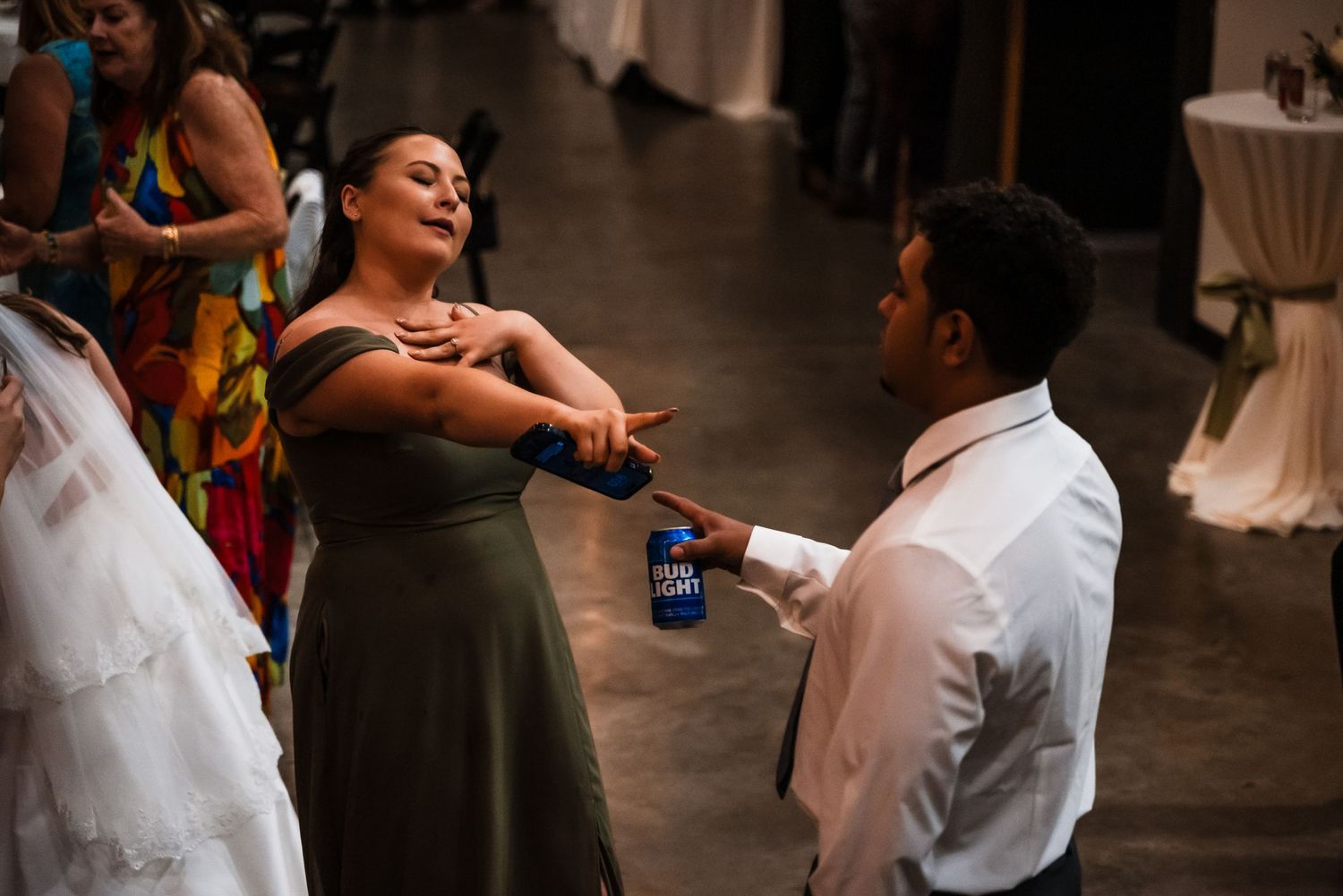 Two people on a dance floor share an animated conversation while holding drinks at what appears to be a celebration.
