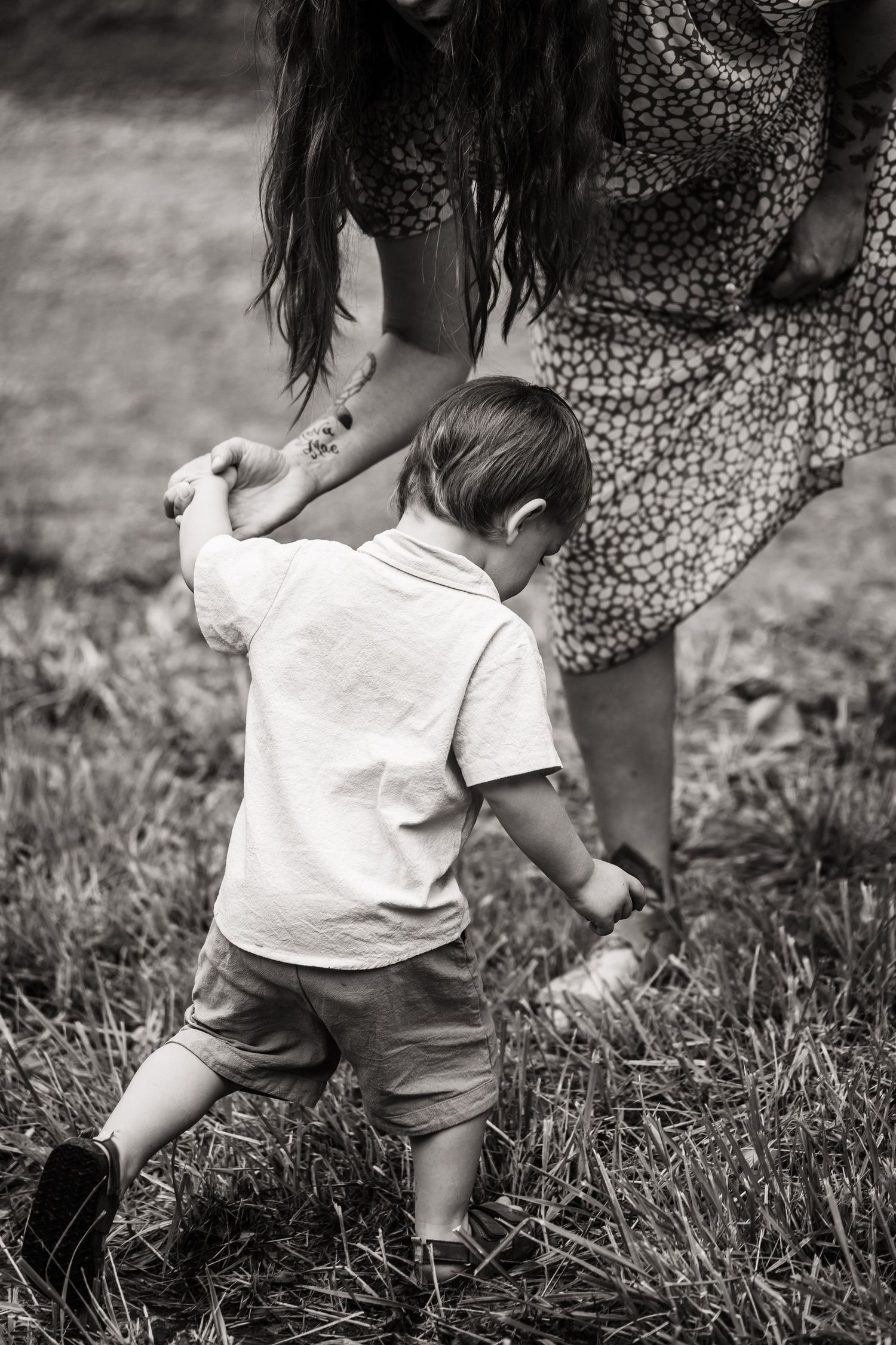 Black and white image of a small child playing in tall grass while wearing a white shirt.