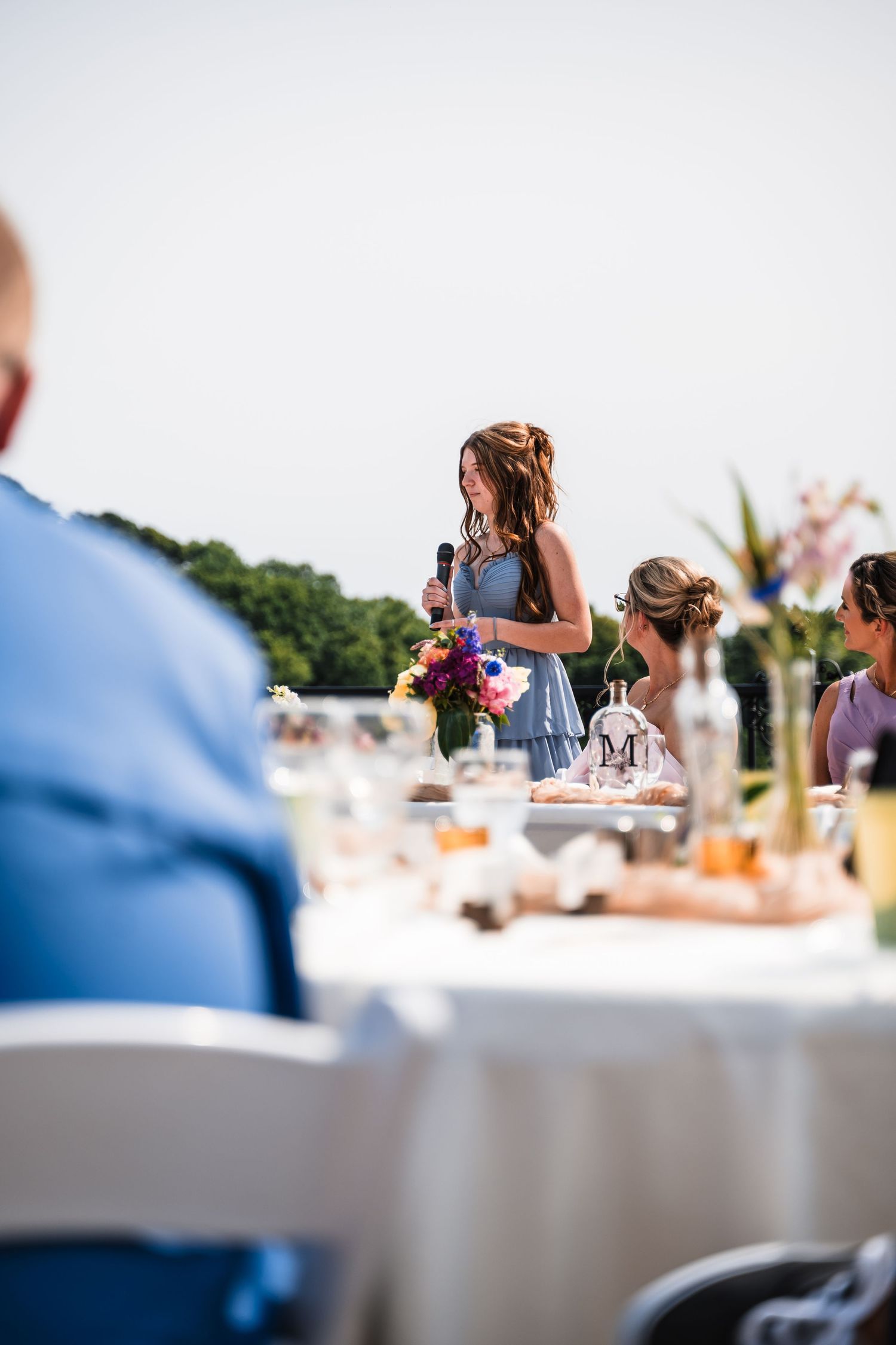 Wedding guests seated at elegant white-clothed tables at an outdoor reception with serene waterfront views.