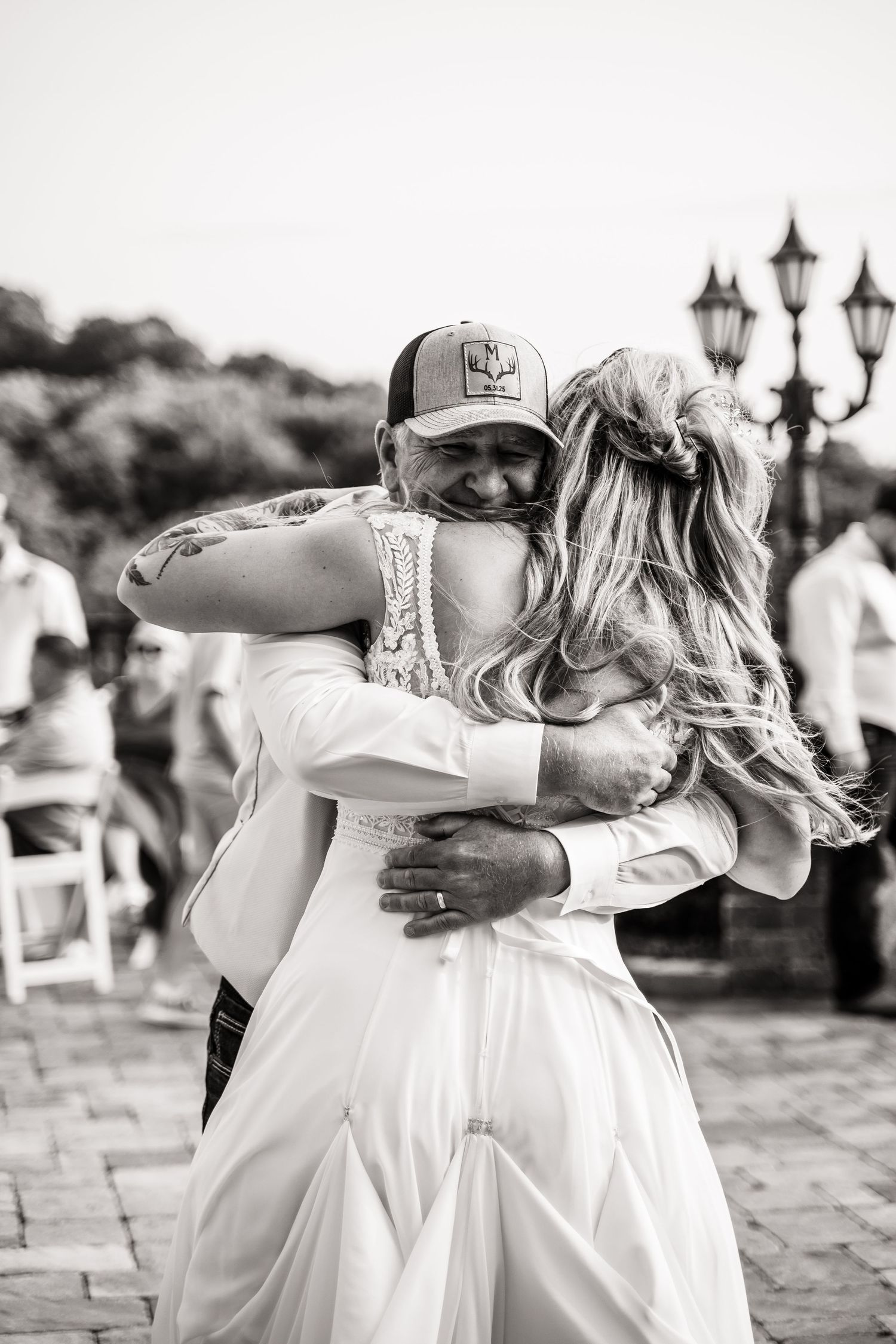 A tender embrace between two people at a wedding celebration with vintage lampposts in the background.