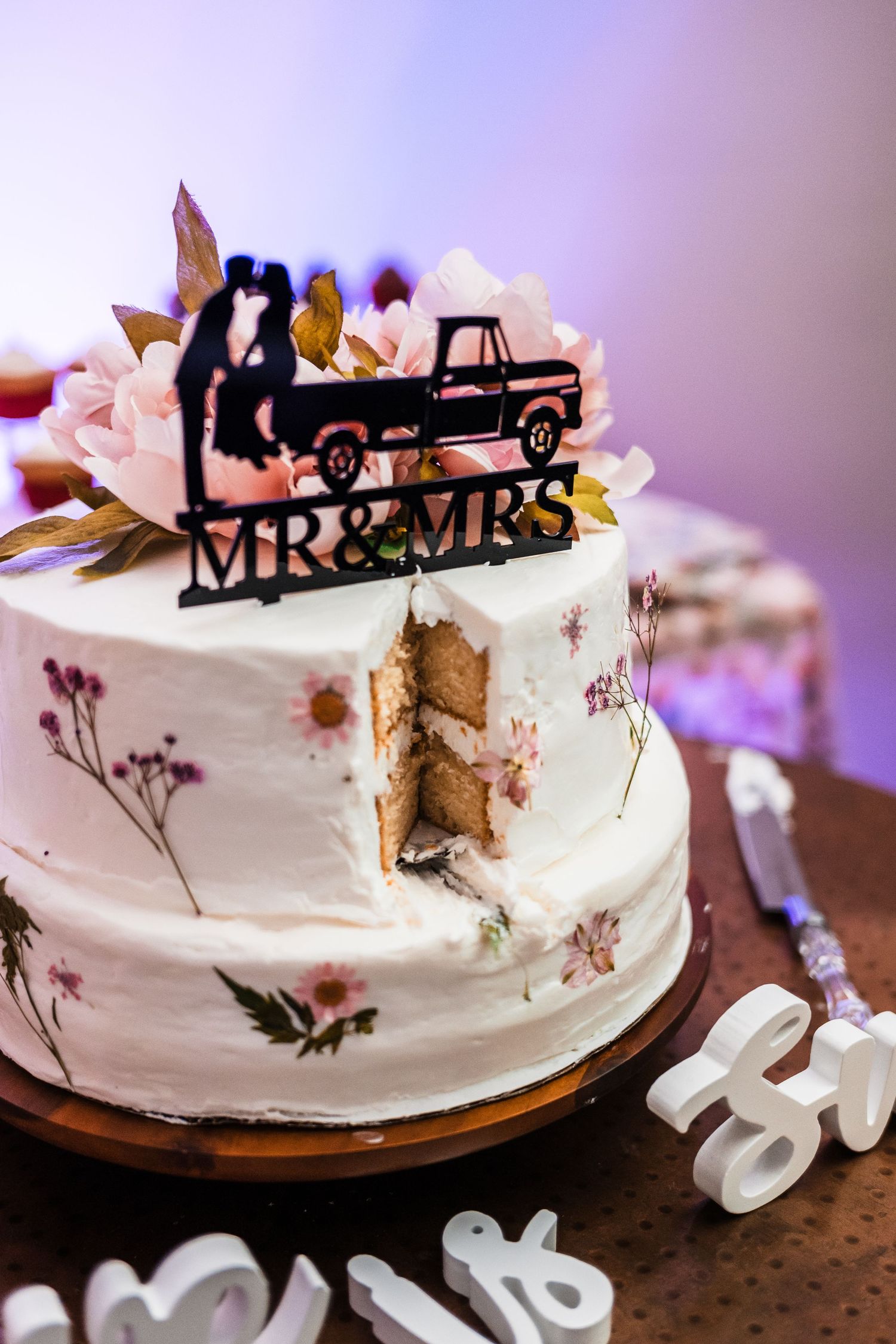 White wedding cake decorated with dried flowers and a Mr & Mrs truck topper silhouette.