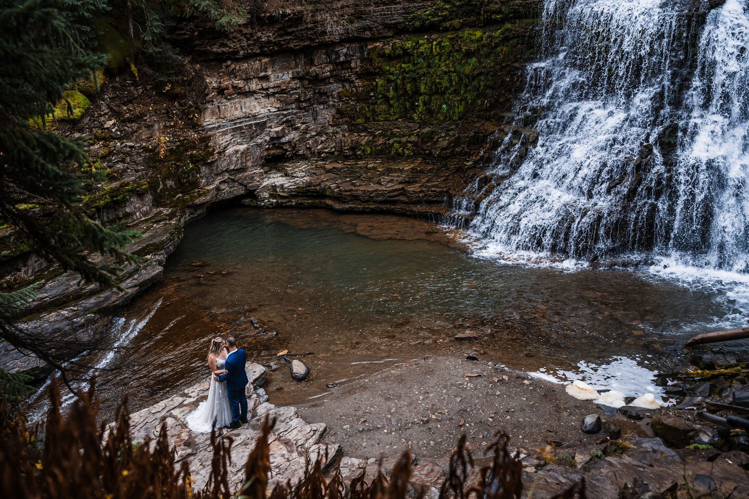 A cascading waterfall creates a stunning natural backdrop for a wedding photo.