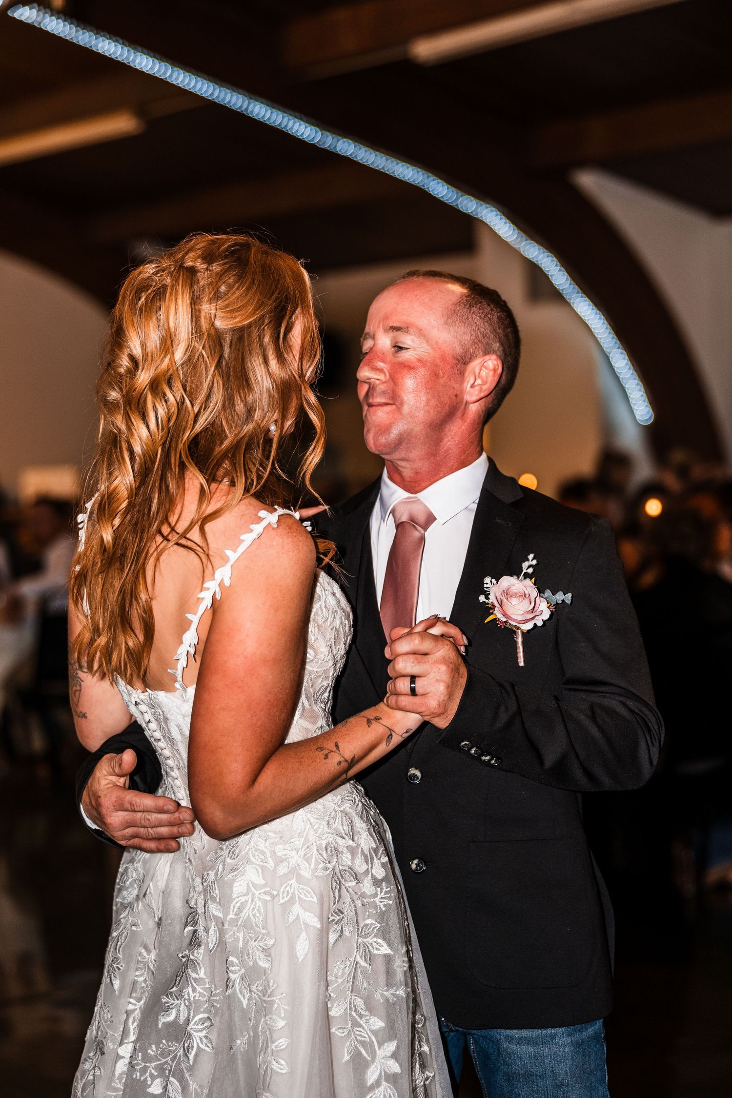 Couple dancing in formal attire at indoor wedding reception with dramatic lighting.