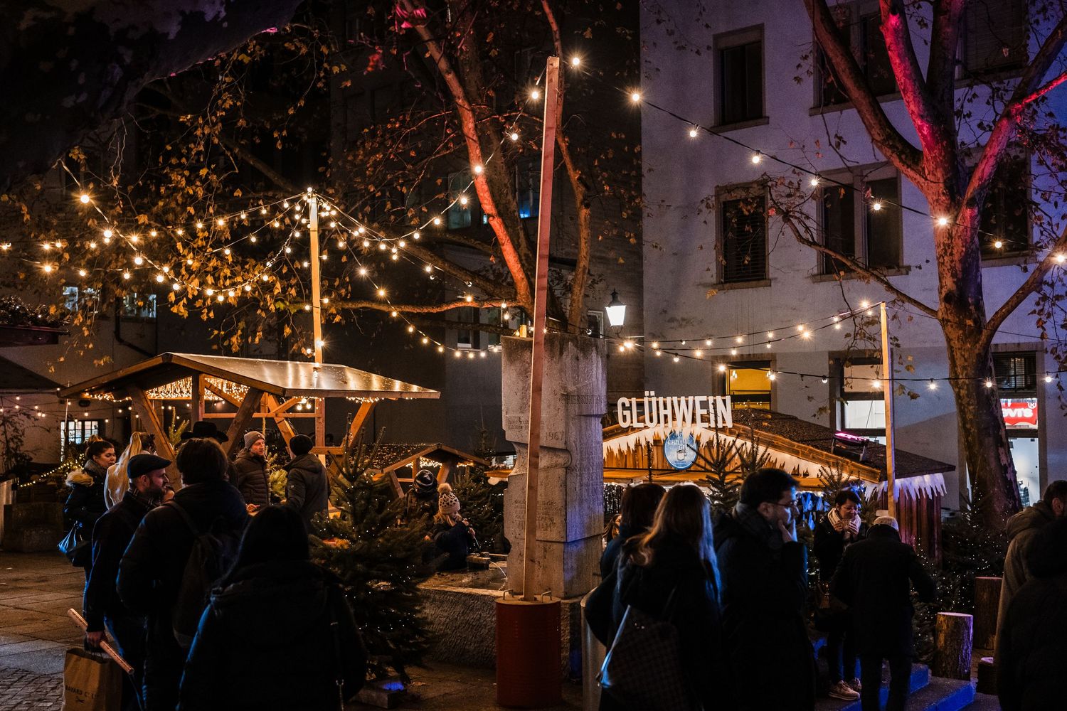 Night market scene with festive string lights illuminating trees and vendor stalls.