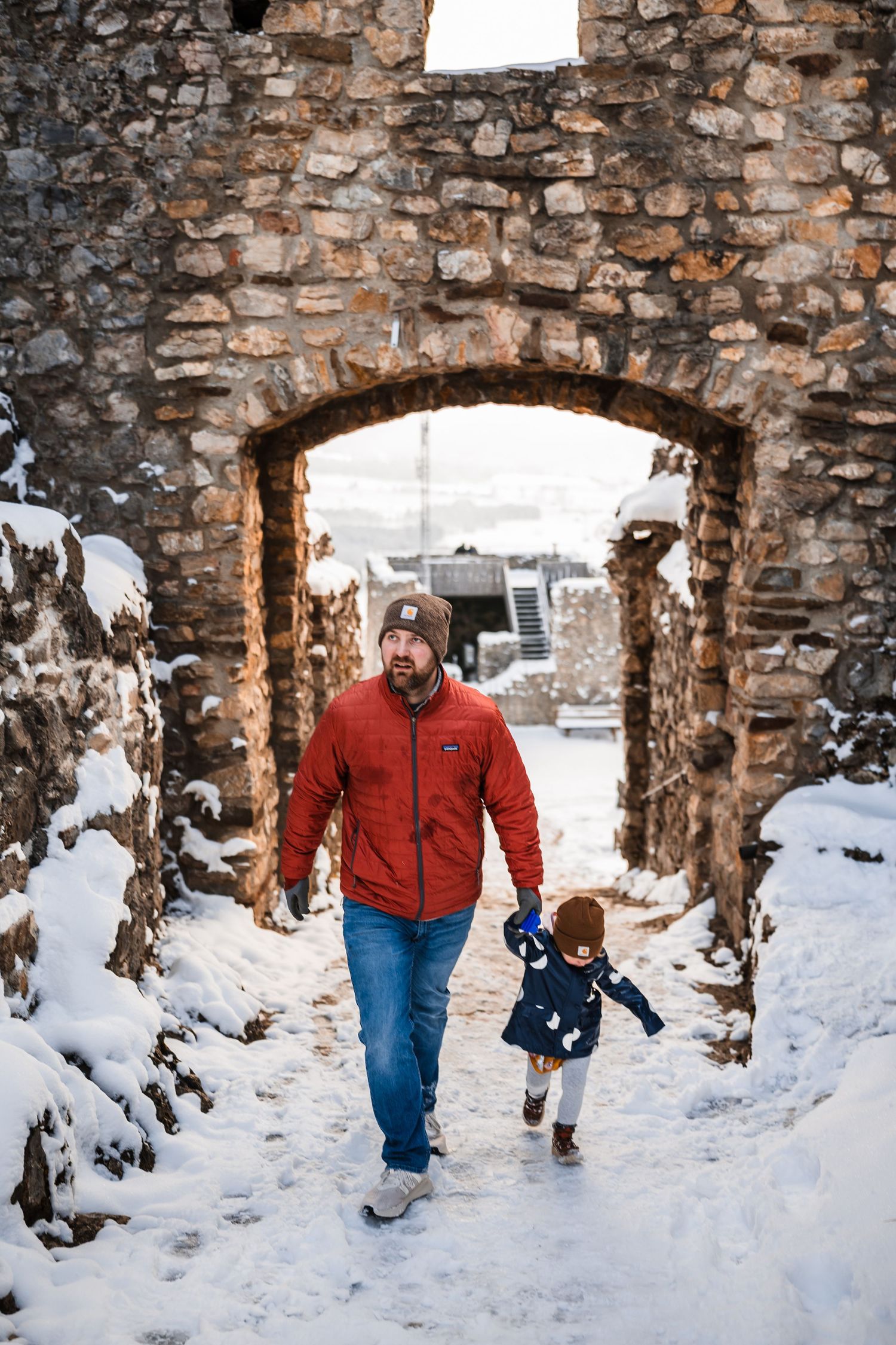 People walking through a snow-covered stone archway passage in winter.