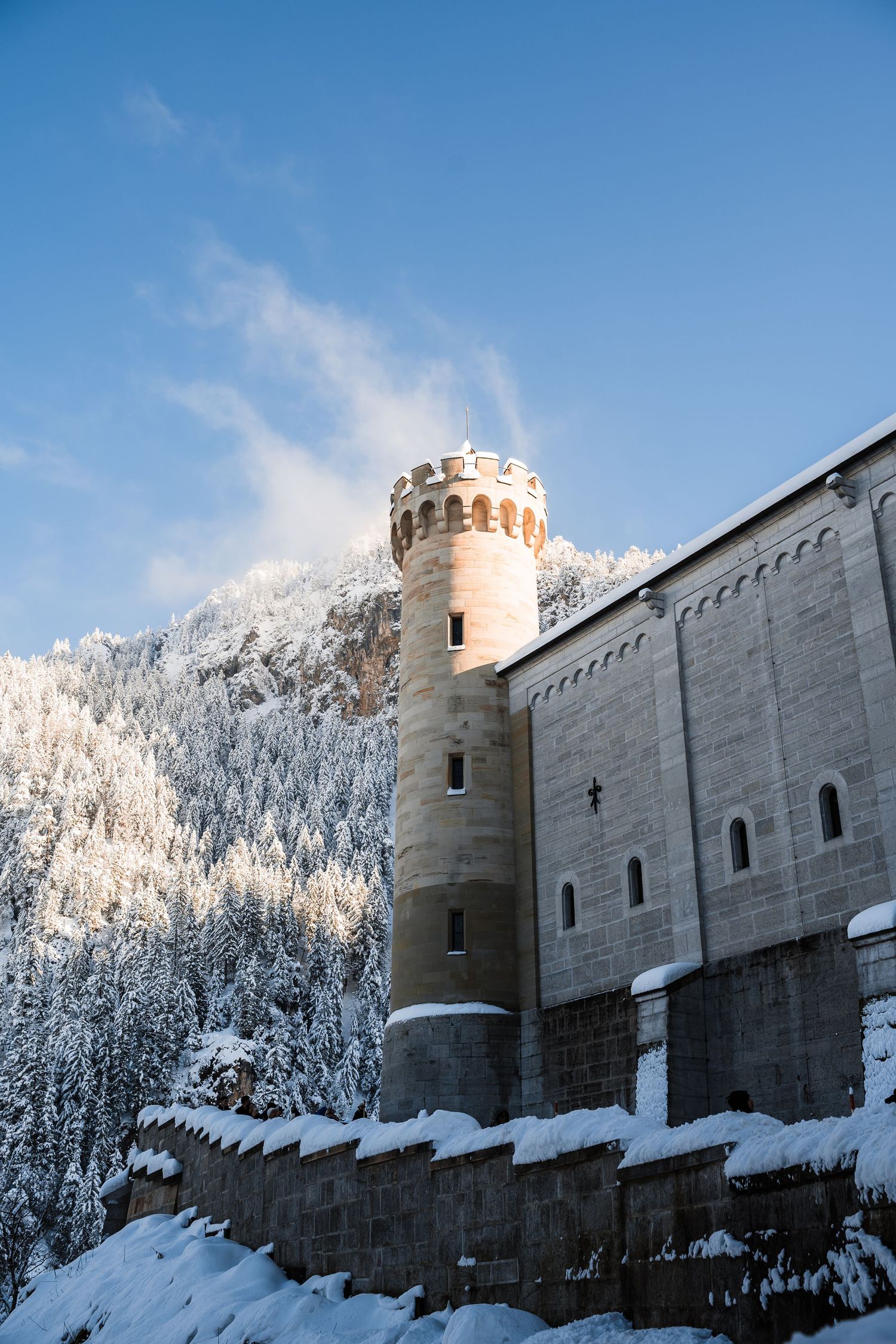 Neuschwanstein Castle's massive stone walls and towers rise above snow-covered winter landscape.