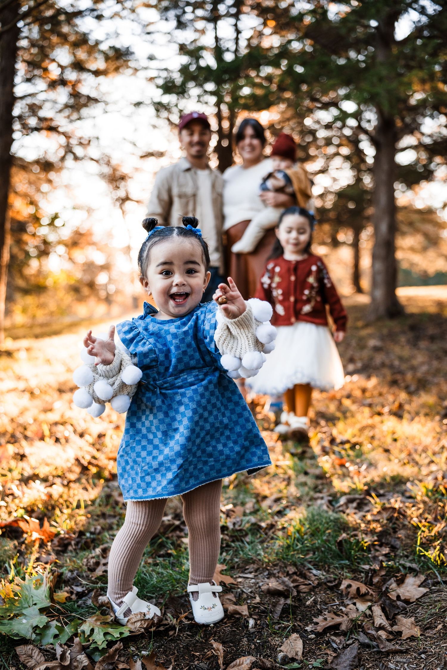 A child in a blue polka dot dress plays joyfully among fallen autumn leaves at sunset.