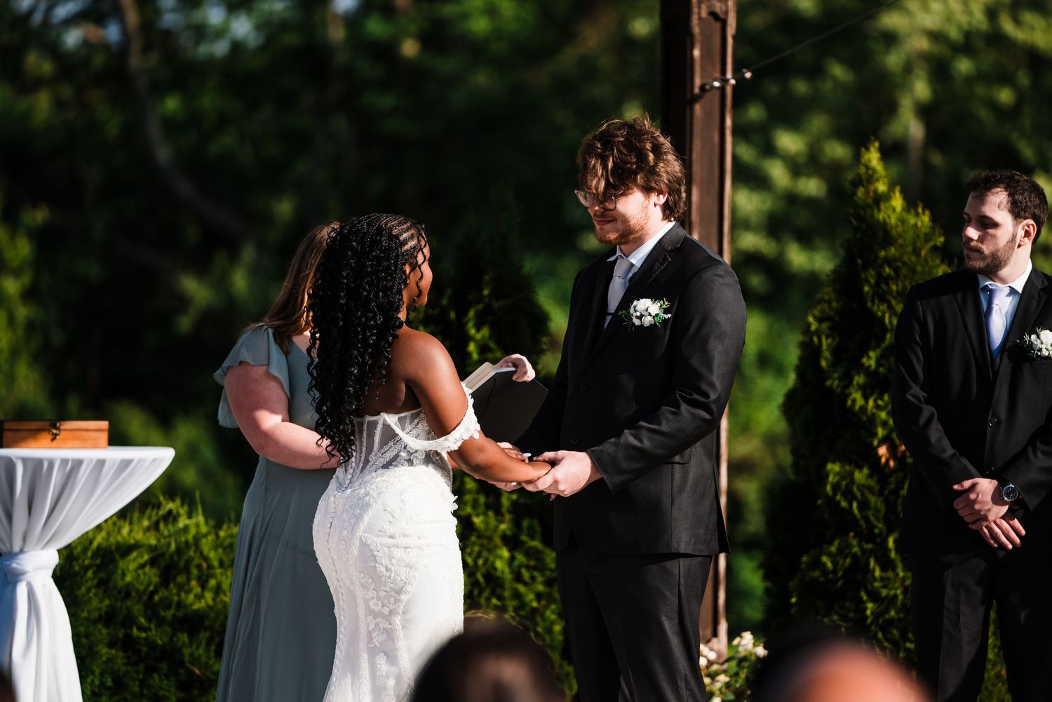 Bride placing ring on grooms finger during outdoor wedding ceremony at sunset.