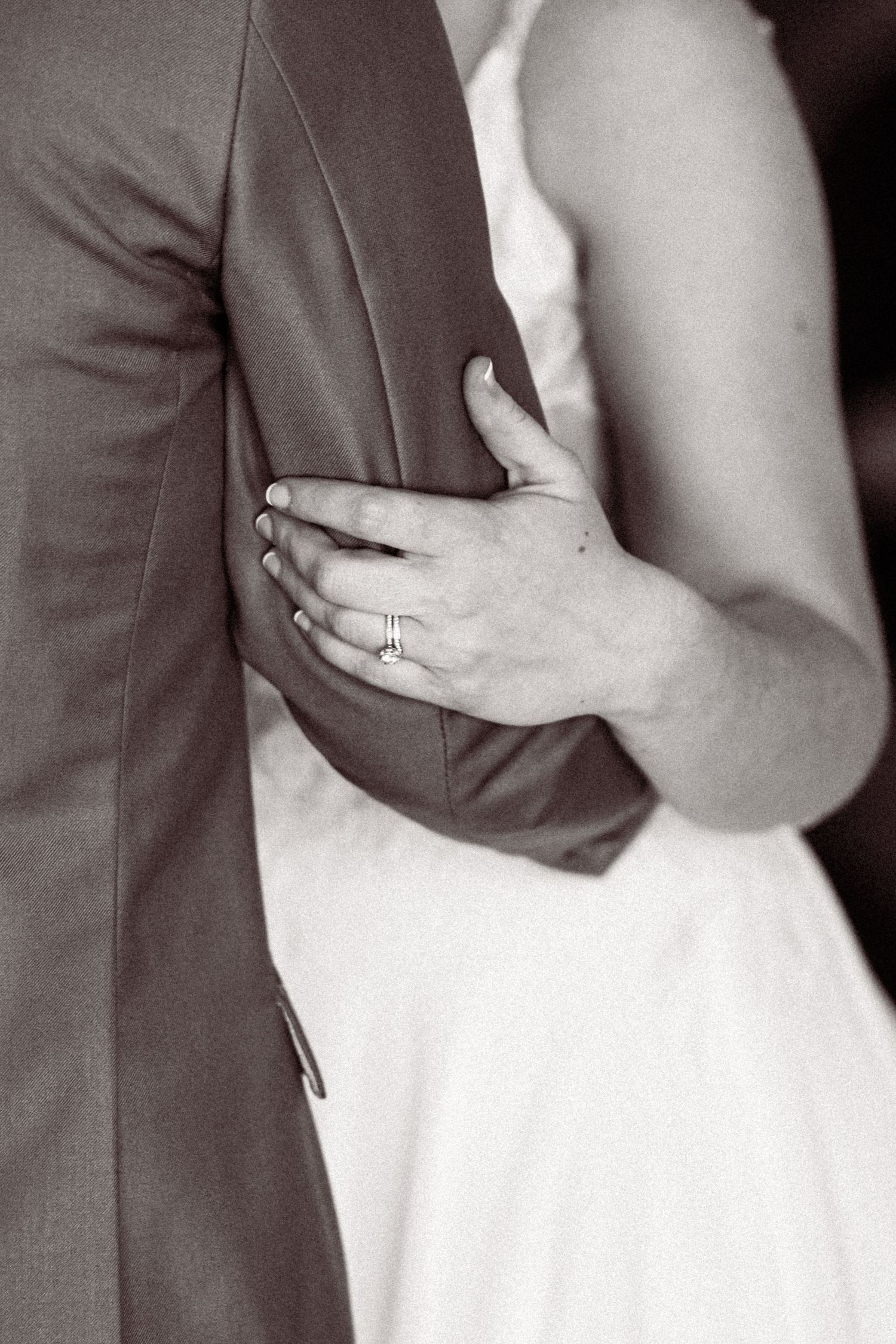 Black and white close-up of bride holding groom's arm, showcasing her wedding ring.