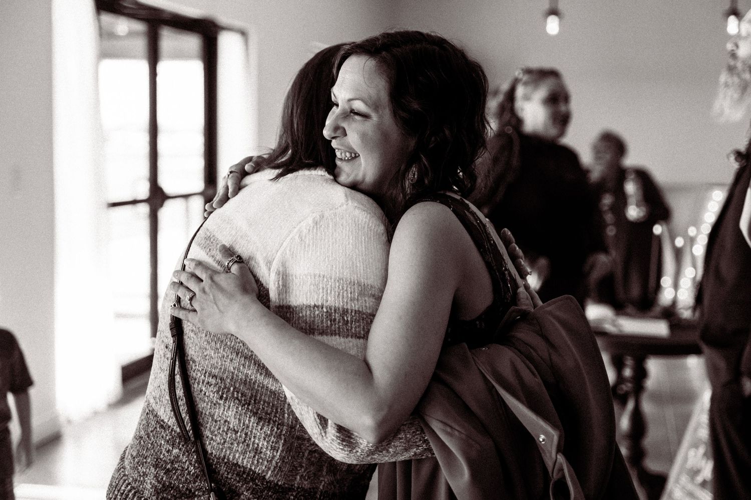 Black and white photo of two women sharing warm embrace at wedding reception venue.