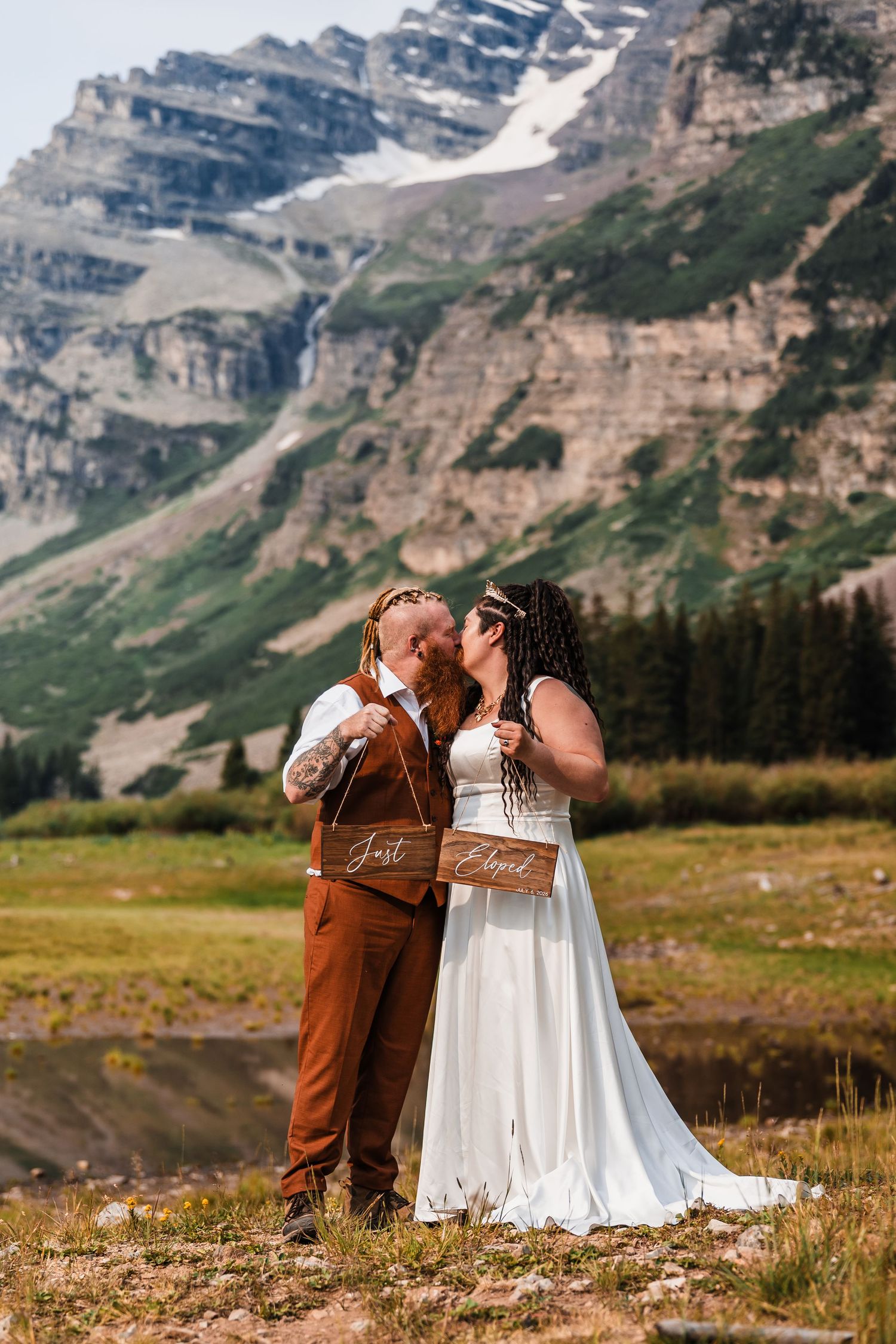 Newlyweds kissing holding Just Eloped sign with snow-capped mountain backdrop in Colorado wilderness.
