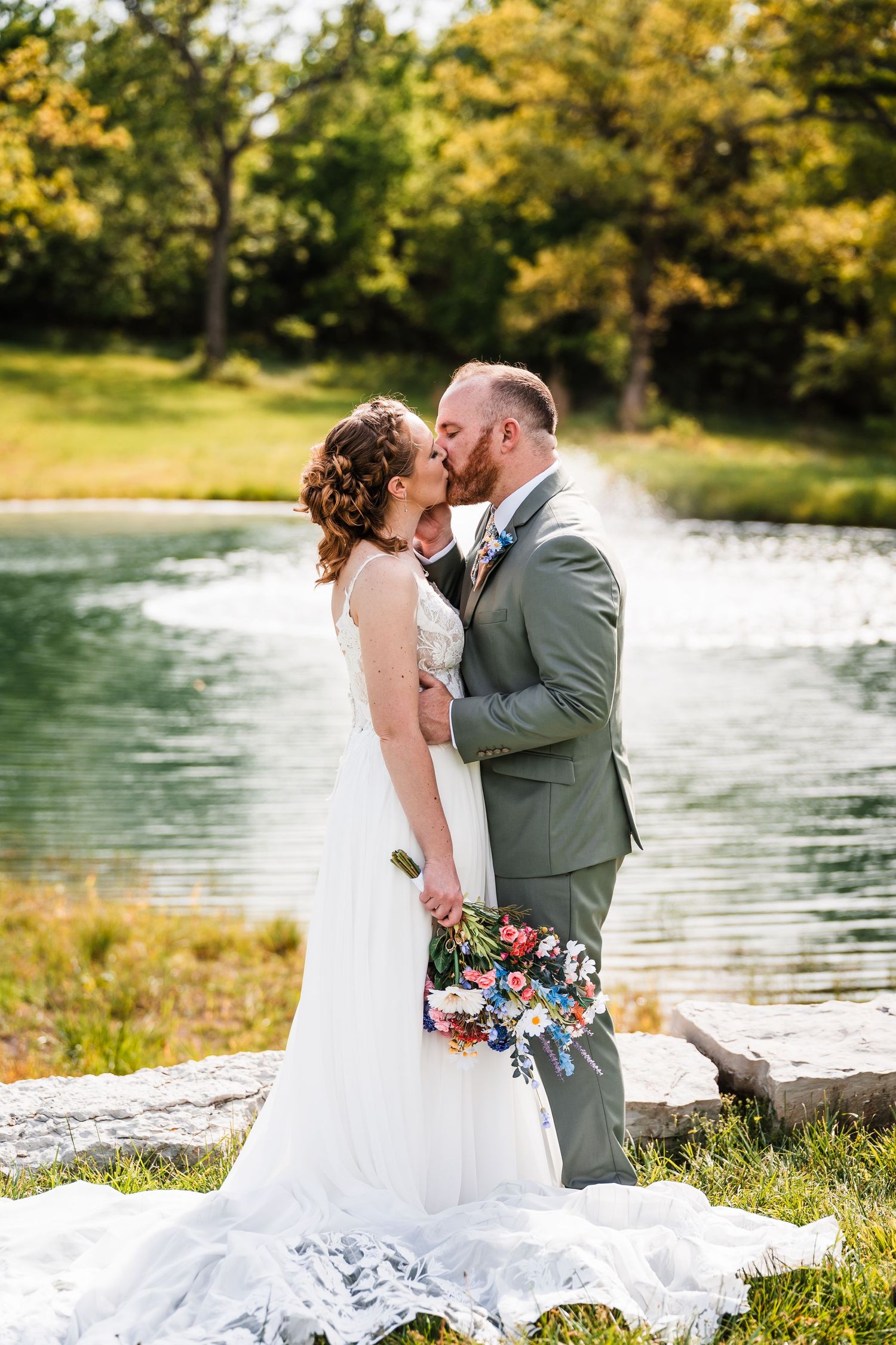 Bride and groom share a romantic kiss by a peaceful pond on their wedding day.
