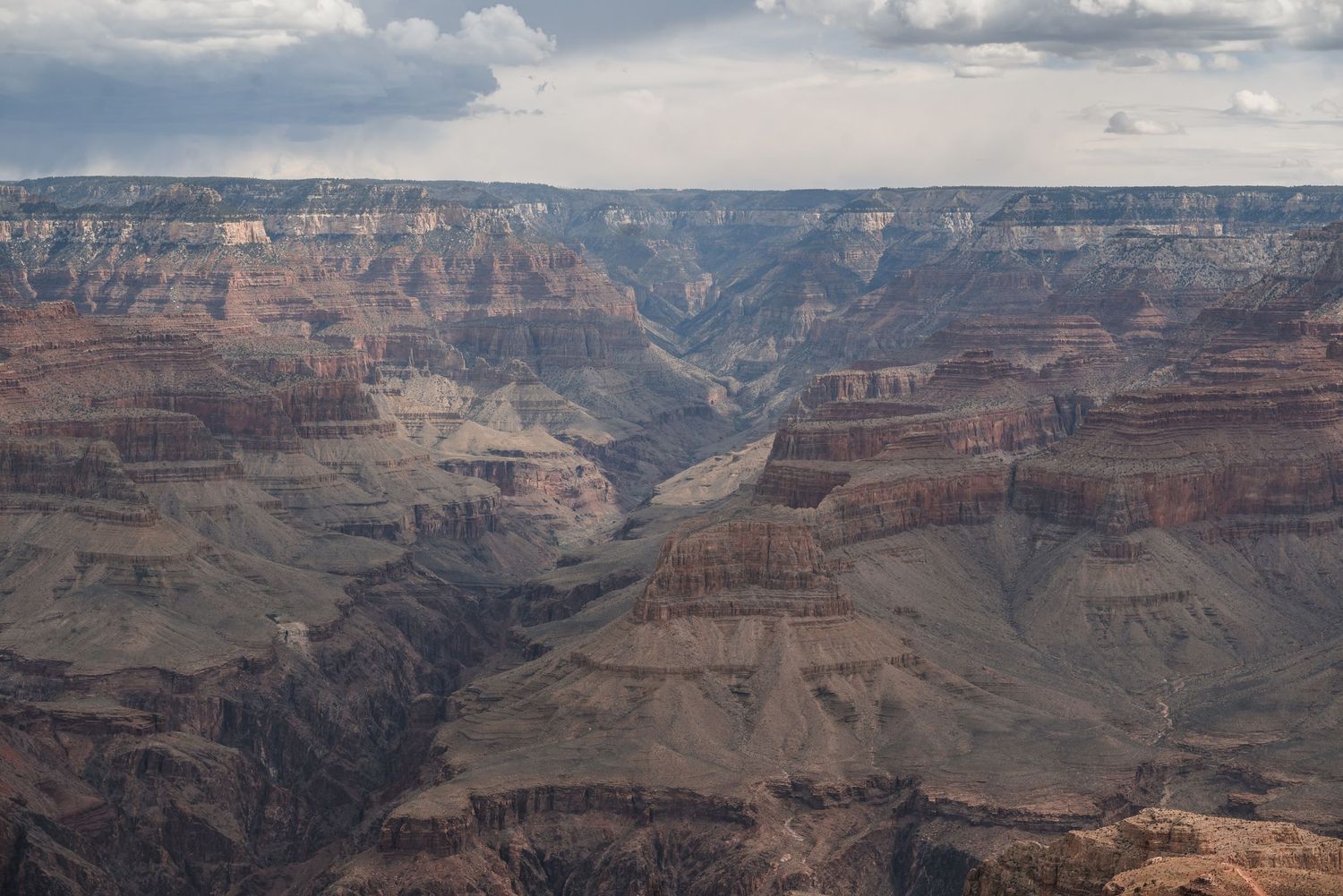 Scenic view of the Grand Canyon with layered red rock formations and winding river valley under cloudy skies.