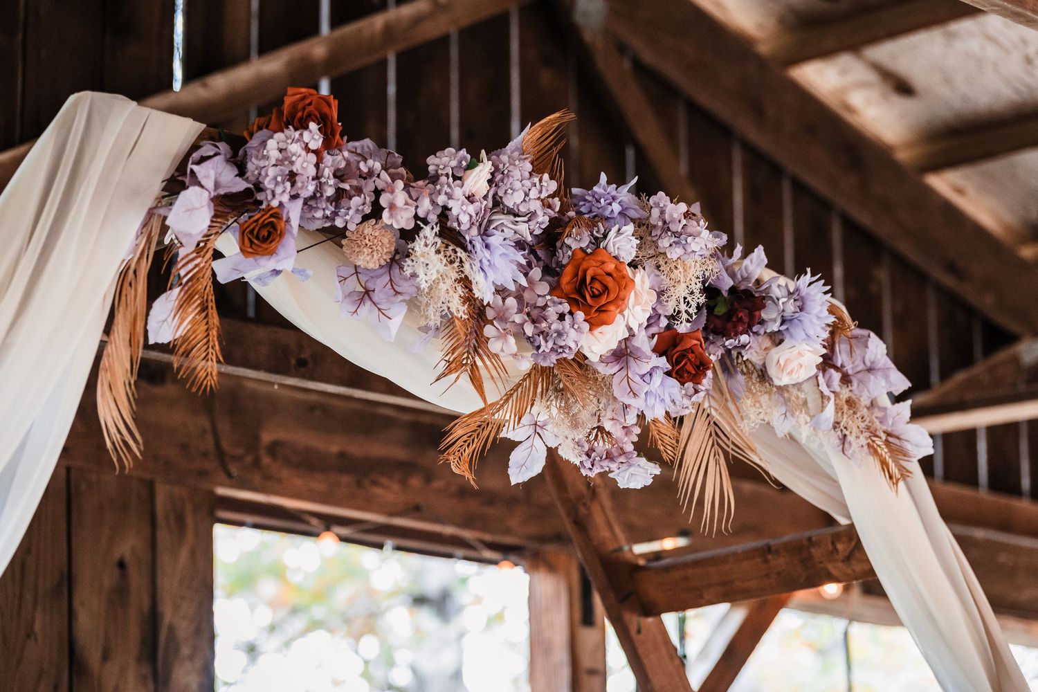 Rustic wooden wedding venue decorated with floral arrangements and white fabric draped from the ceiling.
