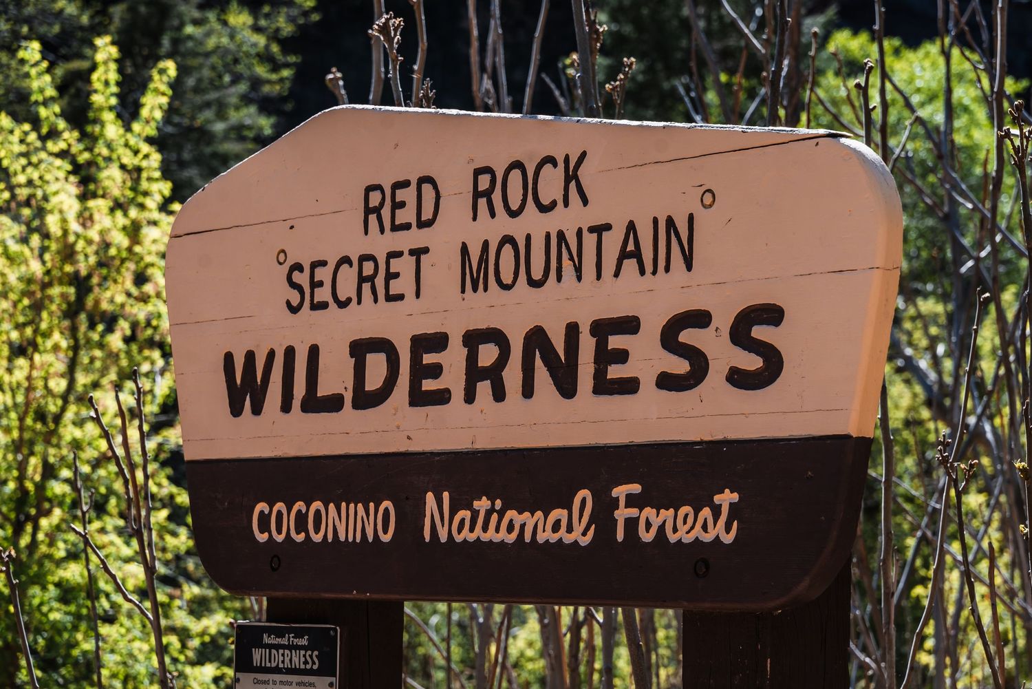 A brown wooden sign marks the entrance to Red Rock Secret Mountain Wilderness in Coconino National Forest.