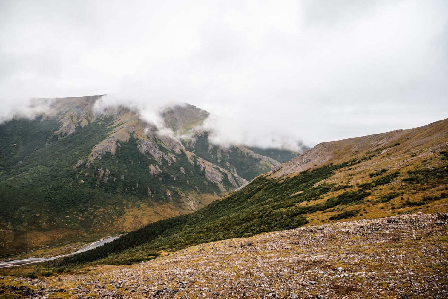 Rocky mountain landscape with low-hanging clouds drifting across rugged peaks and golden autumn slopes.