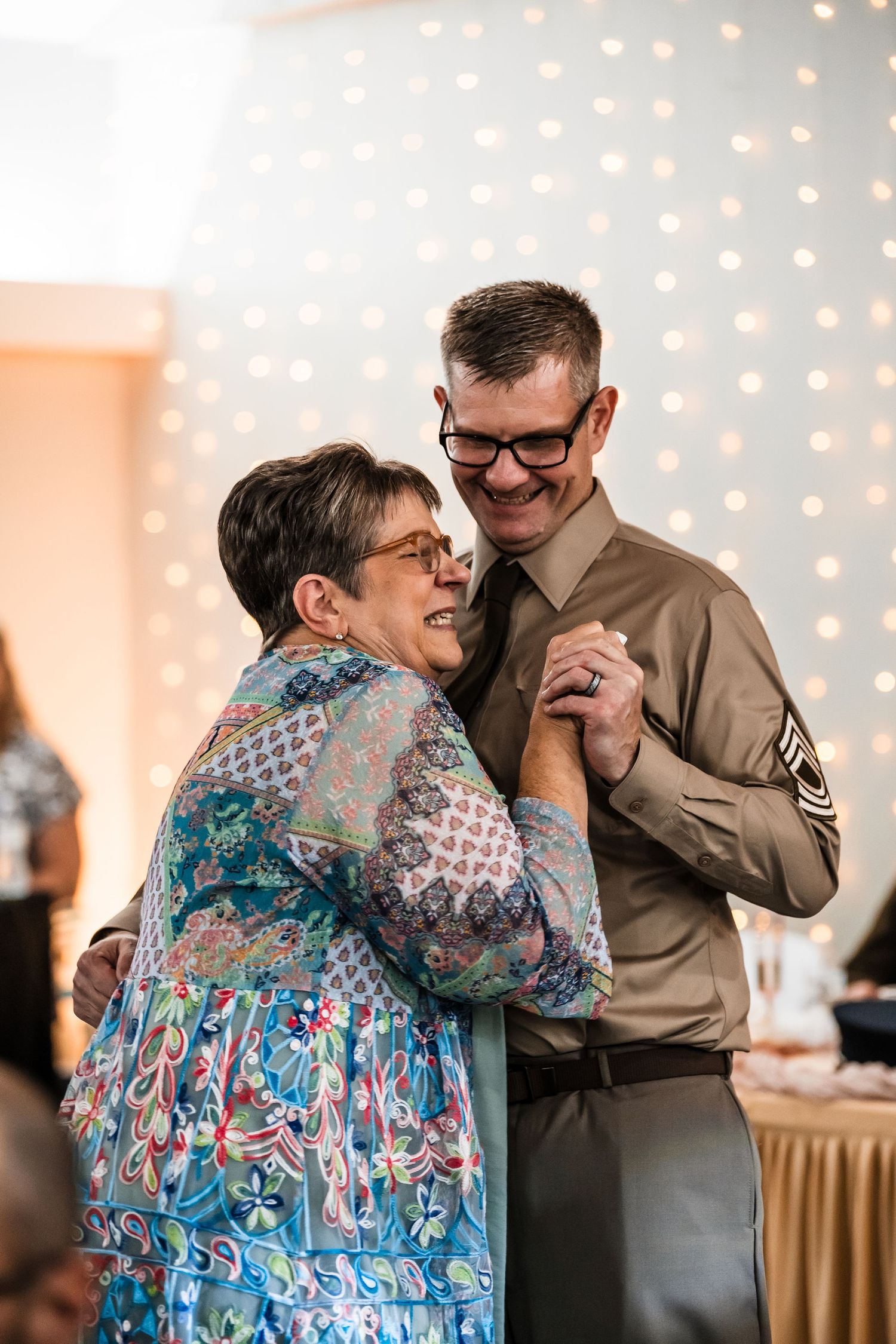 A joyful dance moment captured between two people at a wedding reception with twinkling lights in the background.