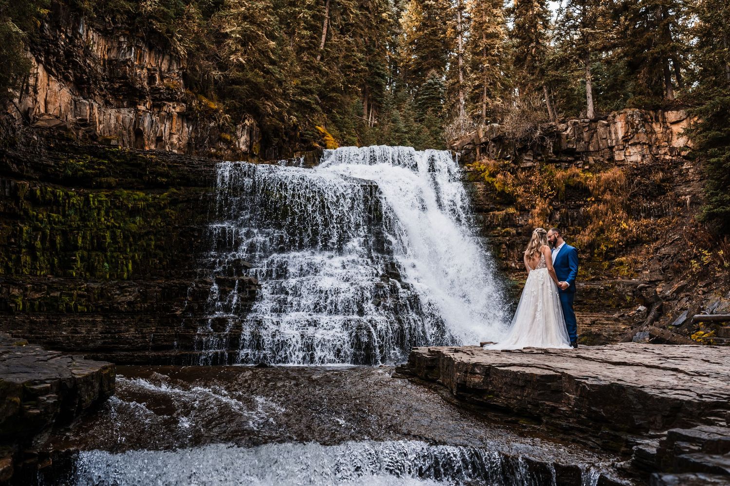 Wedding photography session with scenic waterfall and autumn foliage backdrop.