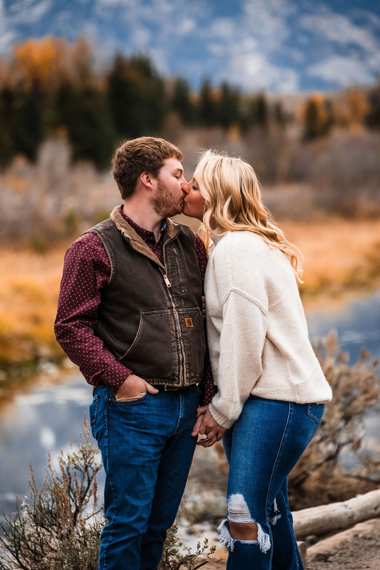 A couple shares tender moments against a scenic mountain backdrop with autumn colors and evergreen trees.