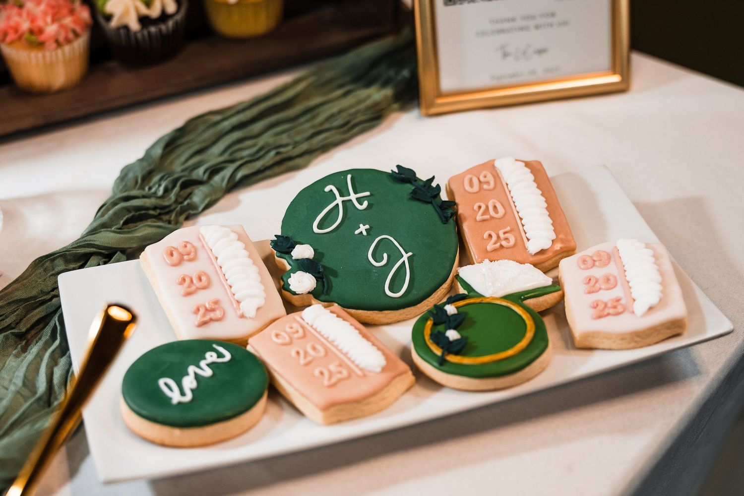 Wedding cookies decorated in green and peach colors displayed on white plates.