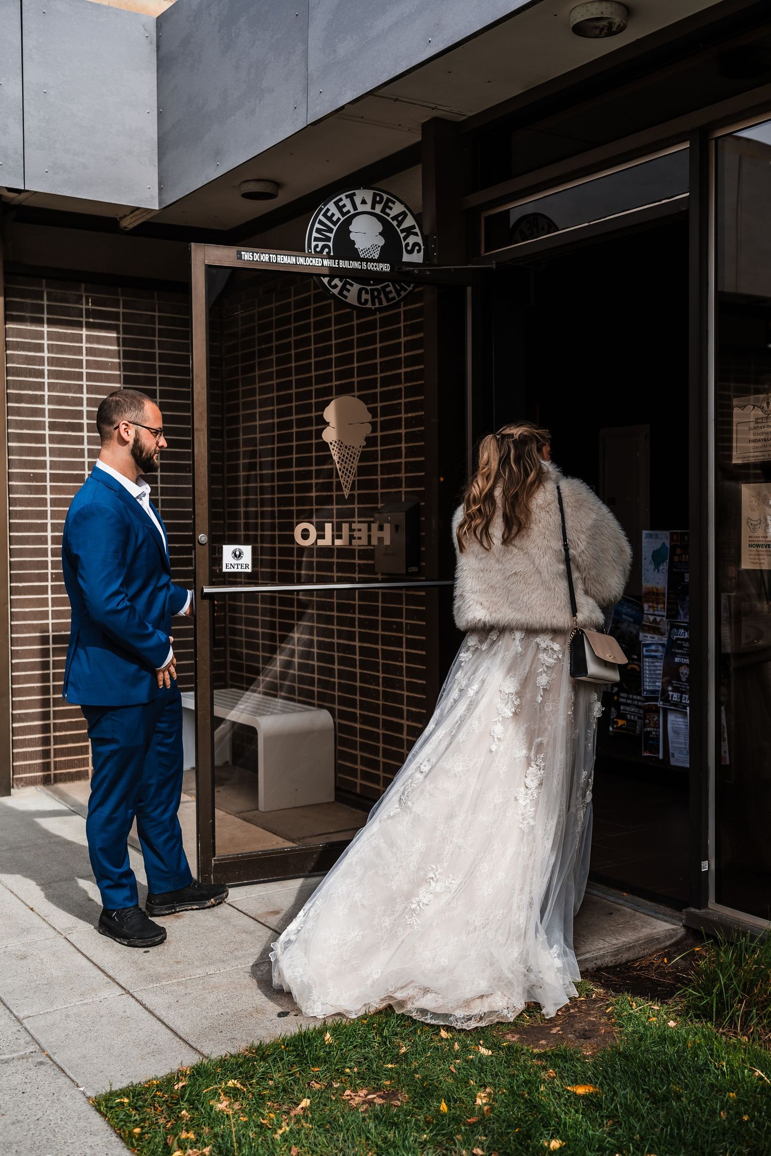 A wedding couple stands outside a storefront with a rustic brick facade.