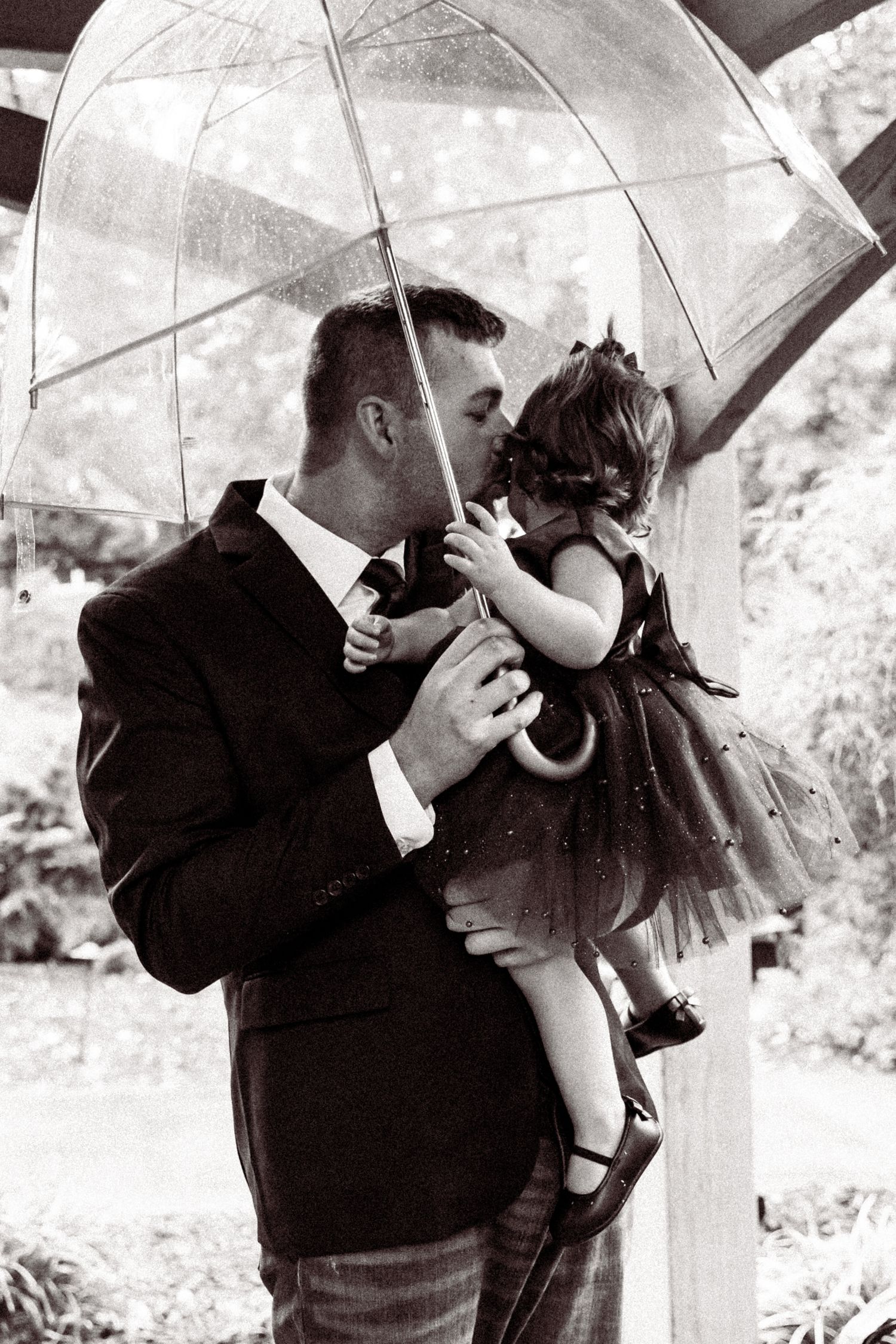 Black and white romantic photo series under clear umbrella in garden setting.