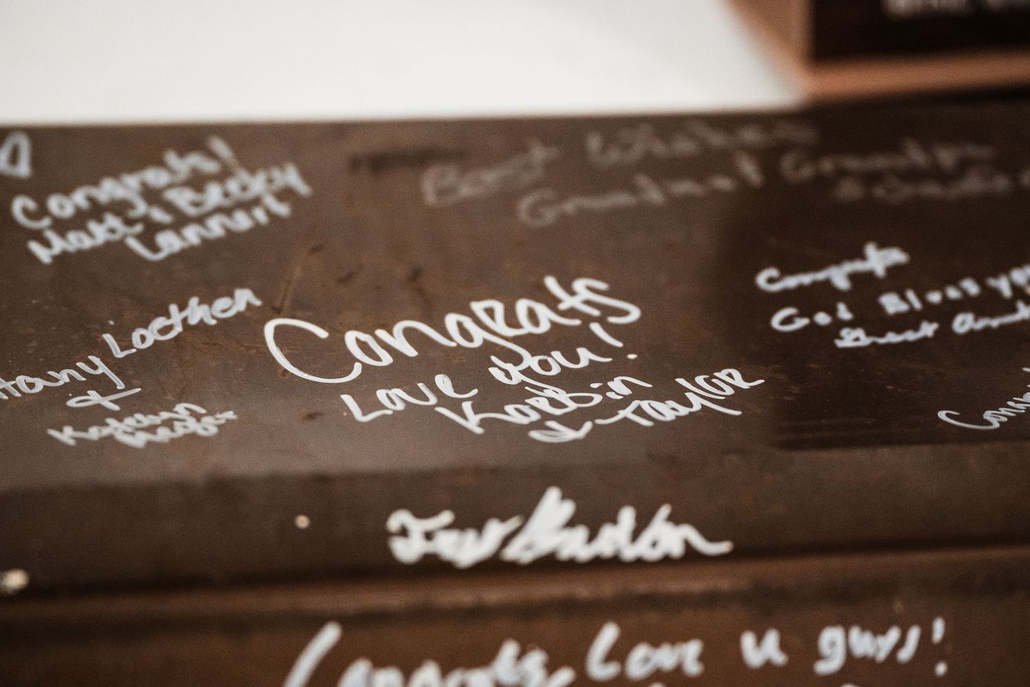 Close up of handwritten signatures and congratulatory messages on a dark wooden surface.