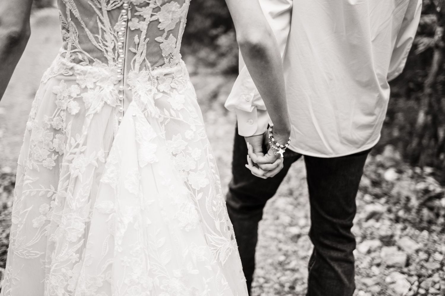 Black and white detail shot of the back of a lace wedding dress and groom's formal attire.