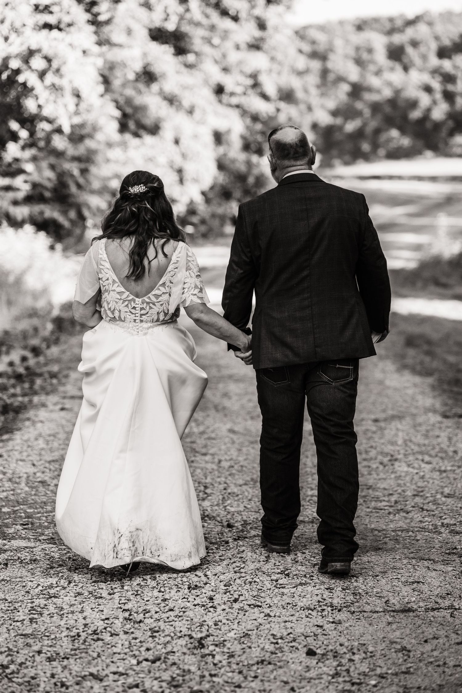 Black and white photo of couple walking down a rustic path in wedding attire.