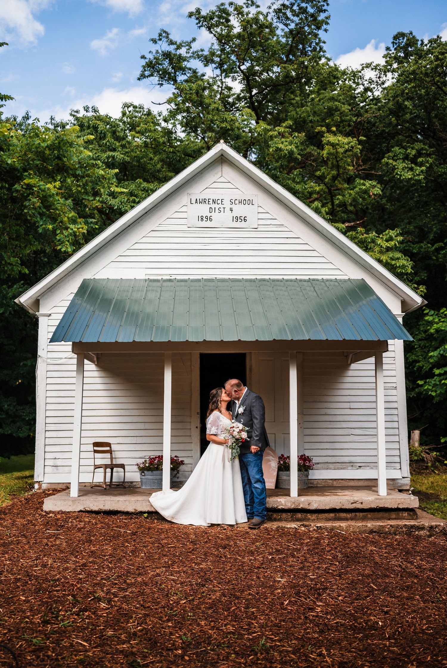 A white-painted schoolhouse building with a front porch is captured in multiple romantic rustic wedding shots on a red clay ground.