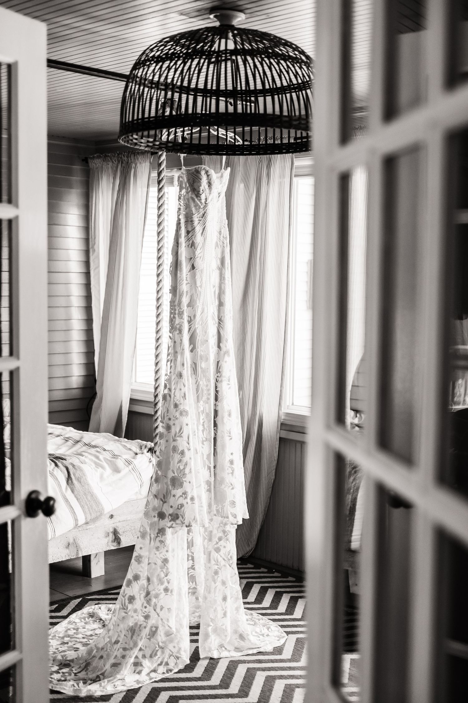 Elegant lace wedding dress hangs from decorative birdcage in black and white.