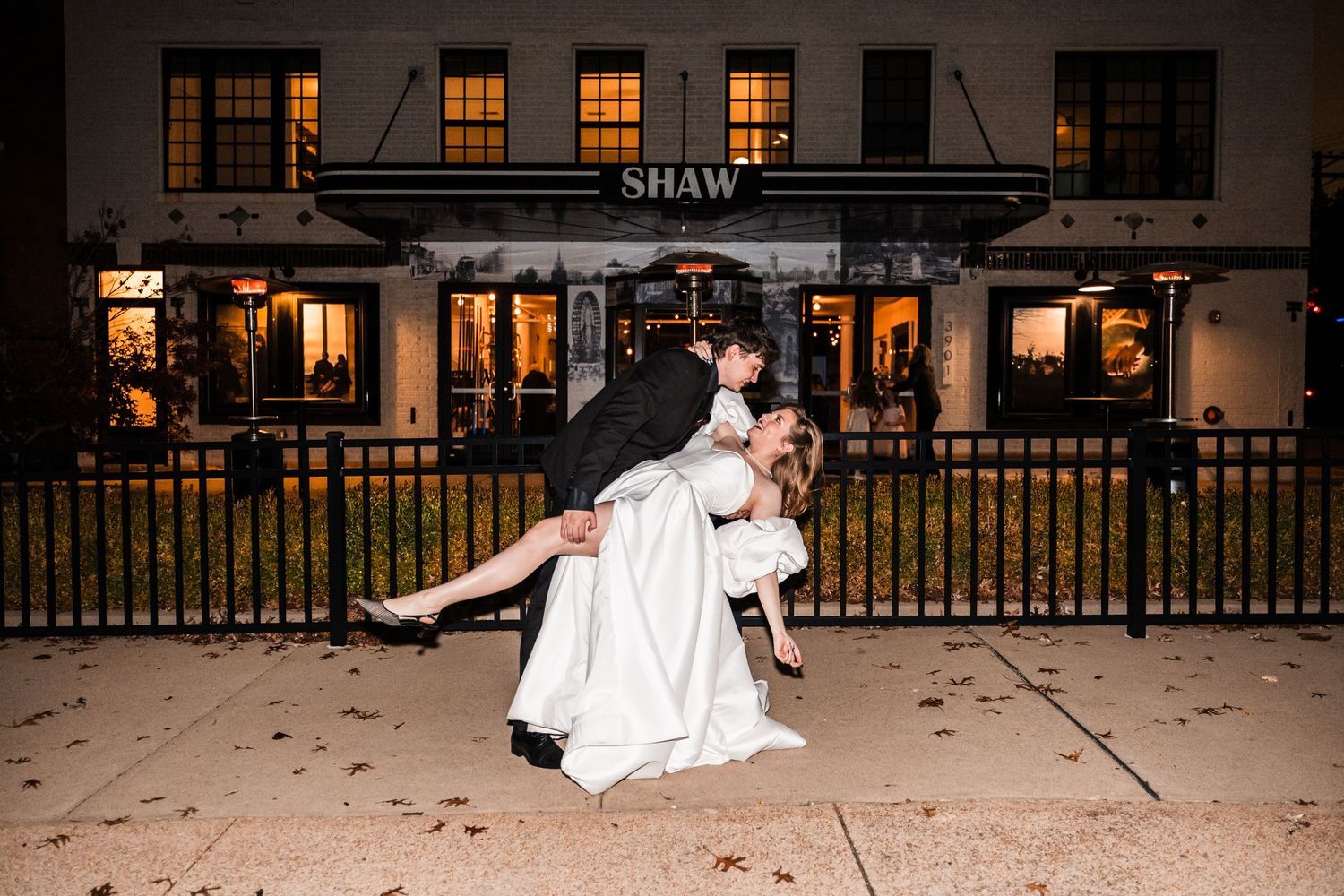 Romantic dip pose captured outside a building with warmly lit windows at night.