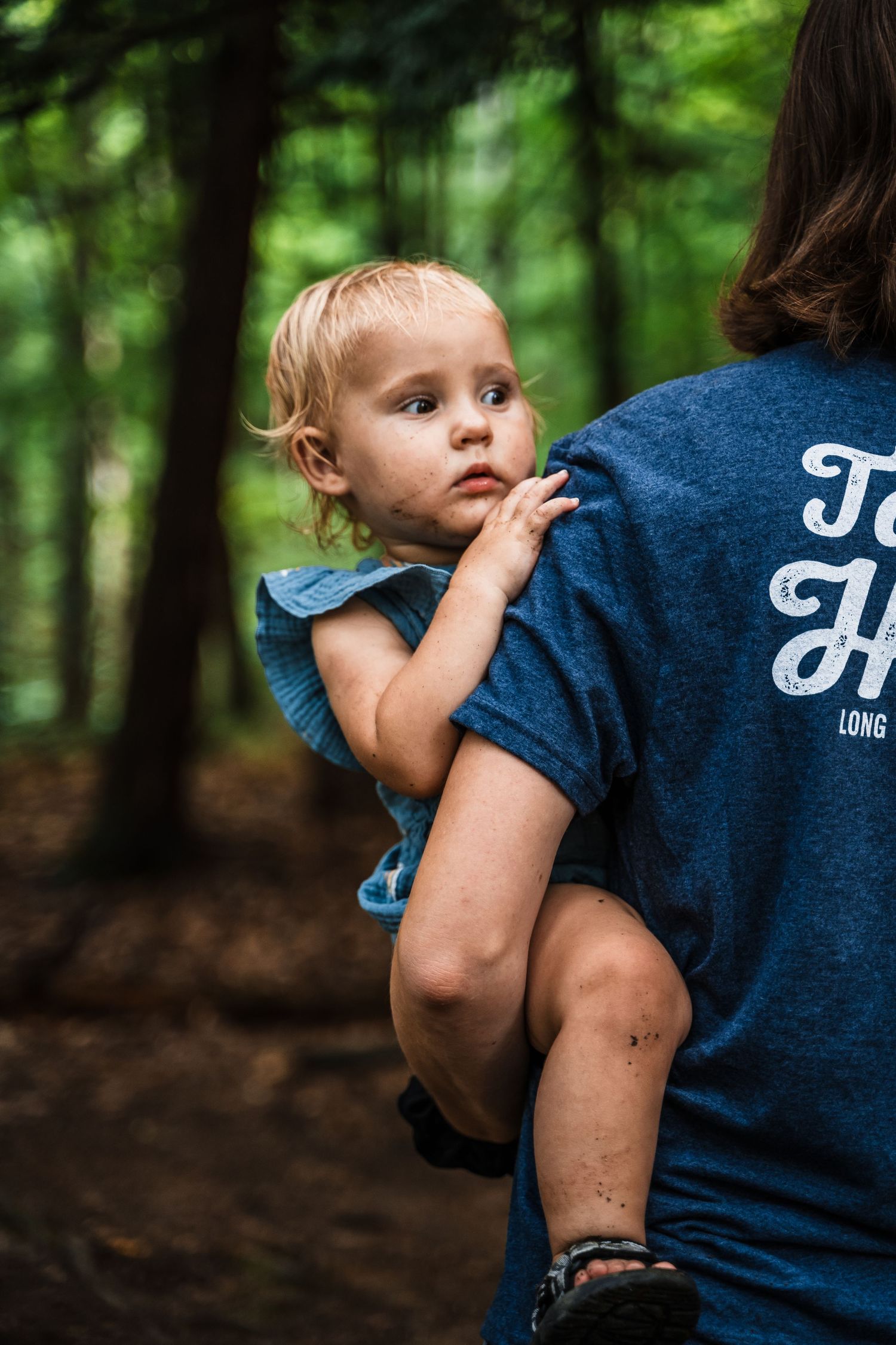 Small child being carried on an adult's back during a forest hike.