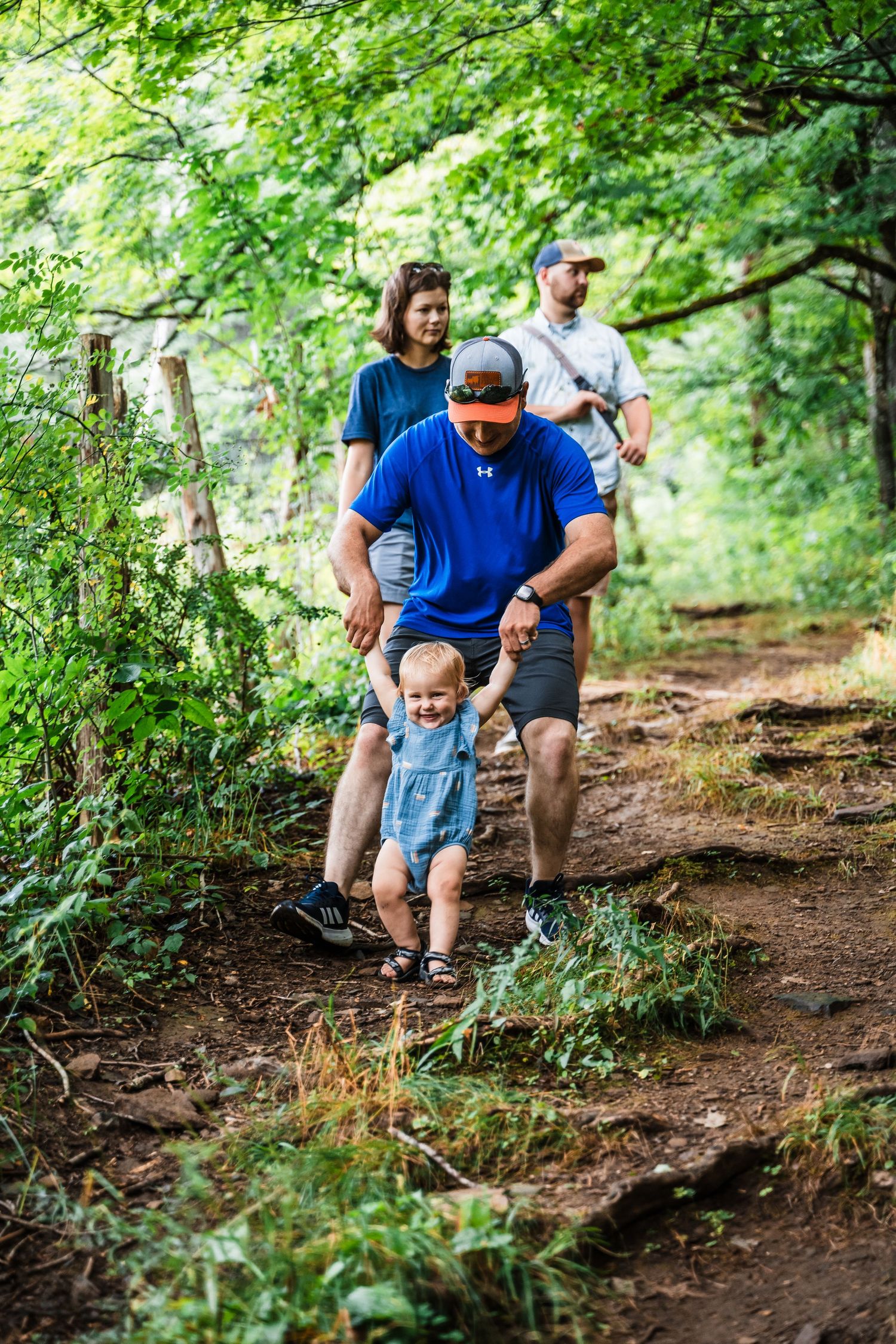 A group of hikers walk along a dirt trail through lush green forest on a summer day.