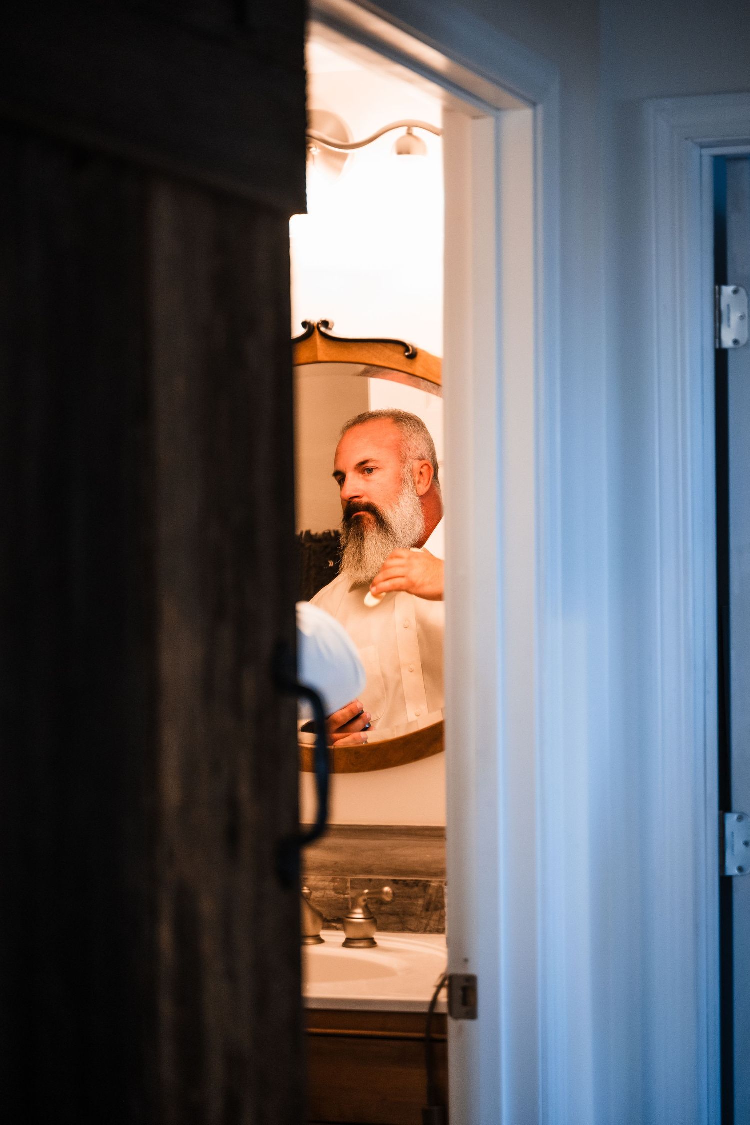 Reflection in bathroom mirror shows person adjusting clothing while getting ready.