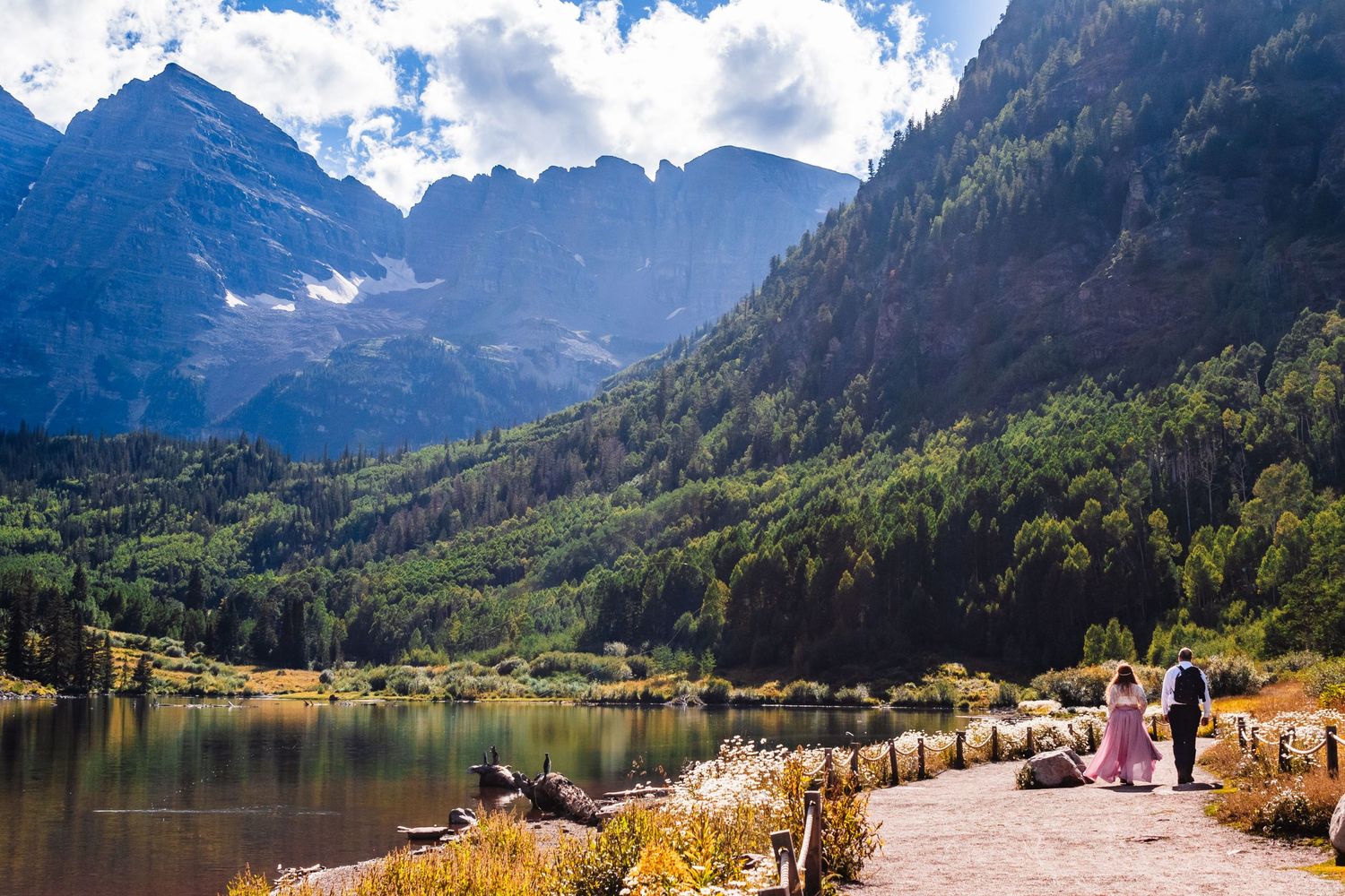 Scenic mountain trail along an alpine lake with distant peaks and hikers enjoying the view.