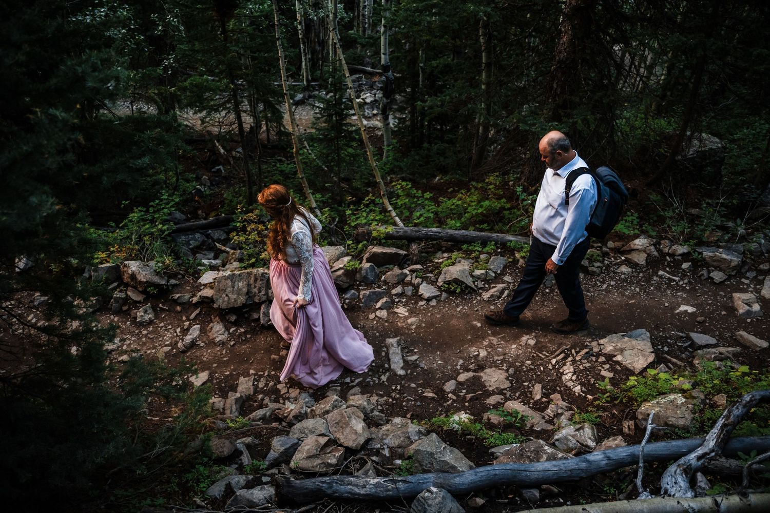 Couple hiking mountain trail through rocky terrain in formal wear.