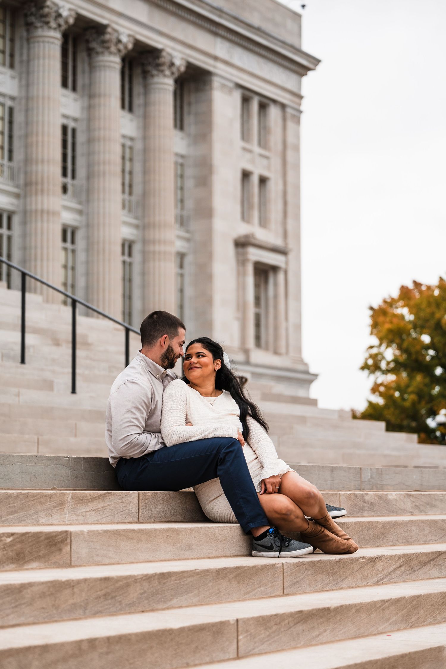 Couple sitting intimately on stone steps of classical building during autumn.