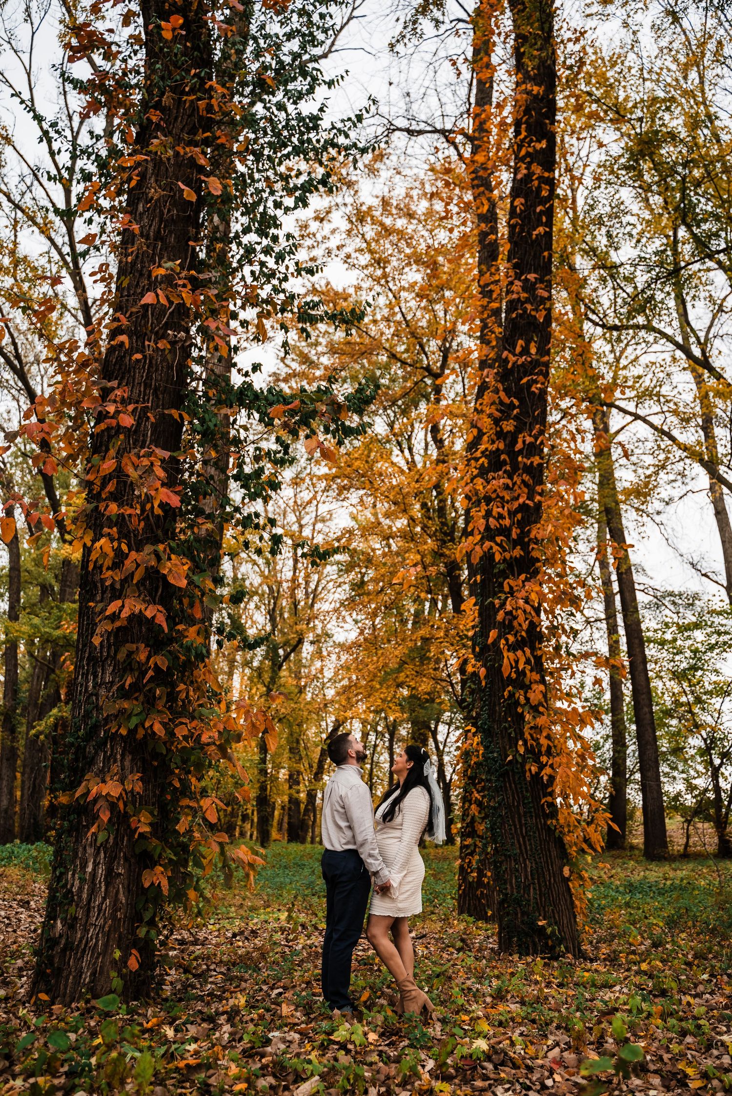 Couple stands close together in beautiful autumn forest setting.