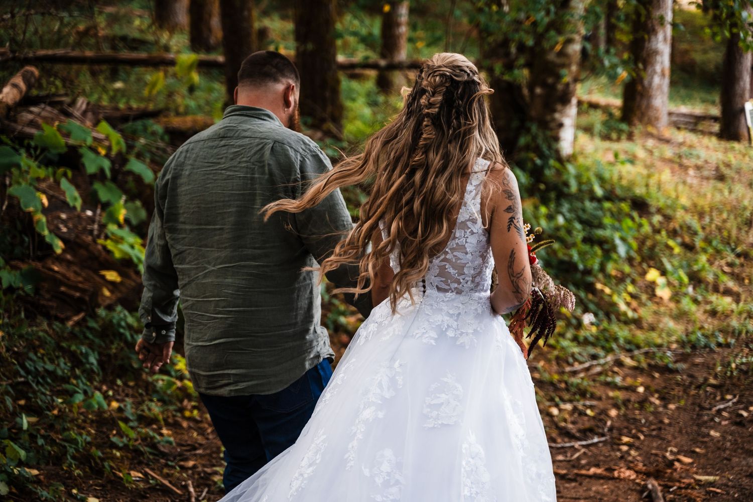 A couple in wedding attire walks along a forest path on their special day.