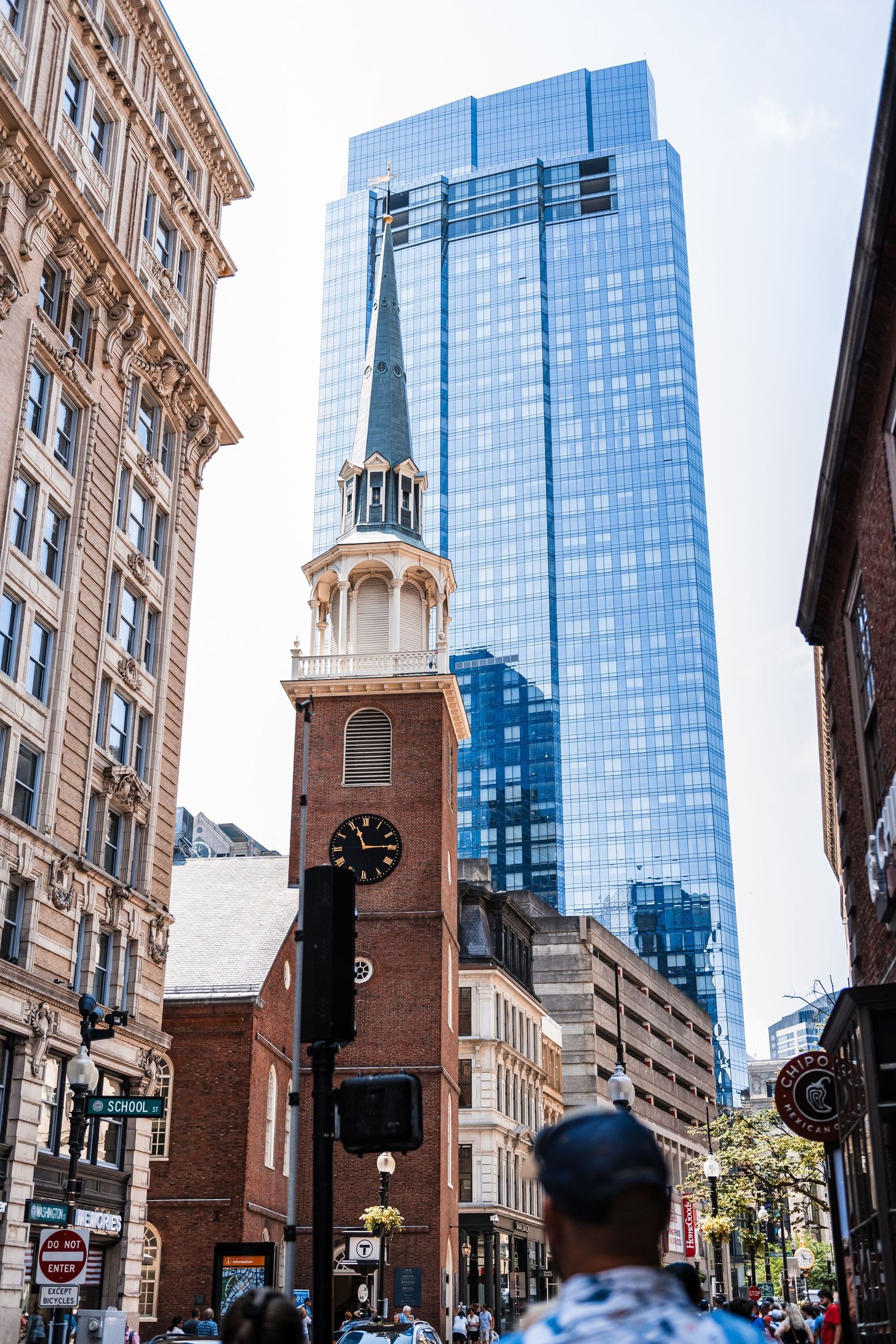 Historic brick clock tower contrasts with modern glass skyscraper in downtown Boston's urban landscape.